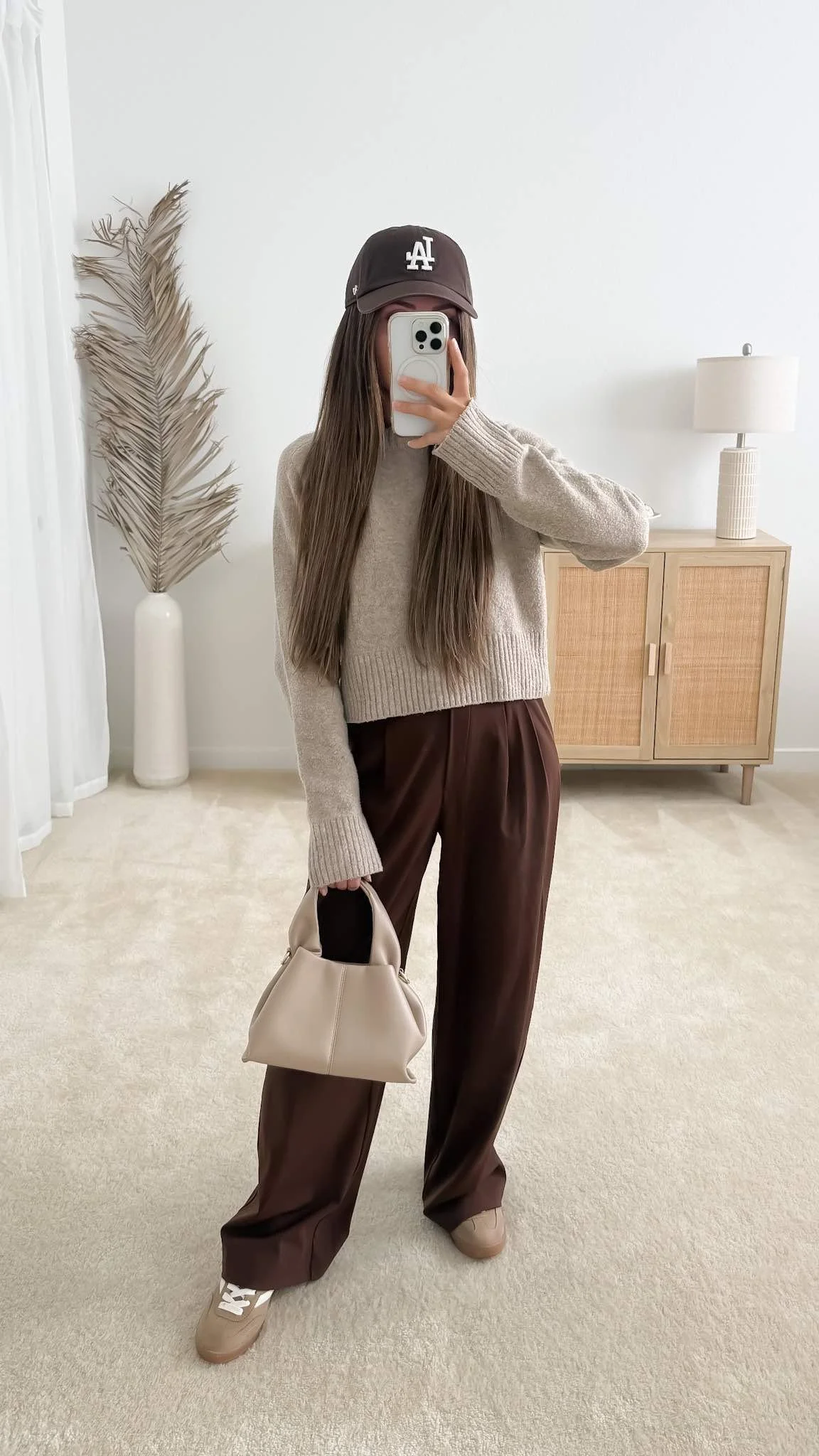Chocolate brown tailored trousers styled with a neutral knit sweater, taupe sneakers, and a cream handbag for fall.
