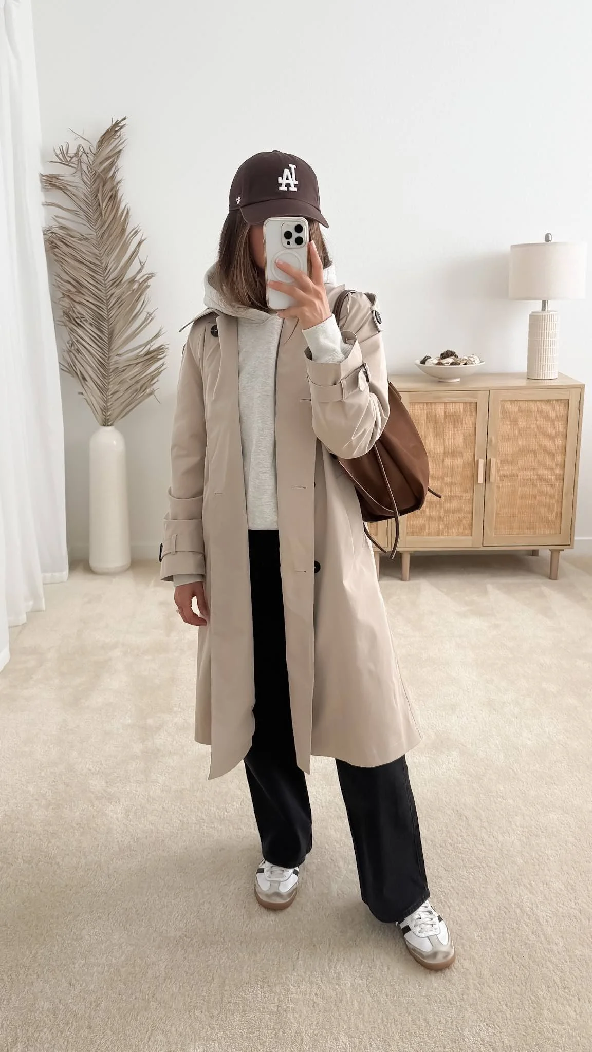 Beige trench coat layered over a gray hoodie with black straight leg jeans and white sneakers for a casual fall outfit.