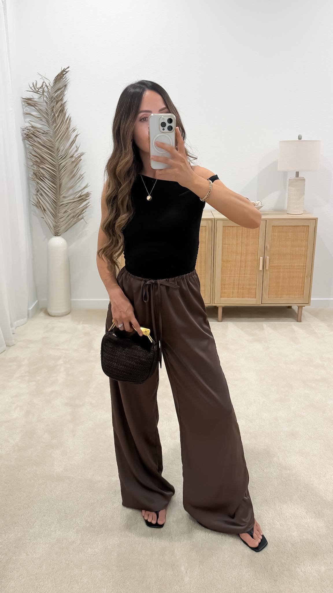 Brown pants outfit with brown satin pants, a black off-the-shoulder top, black sandals, and small black handbag