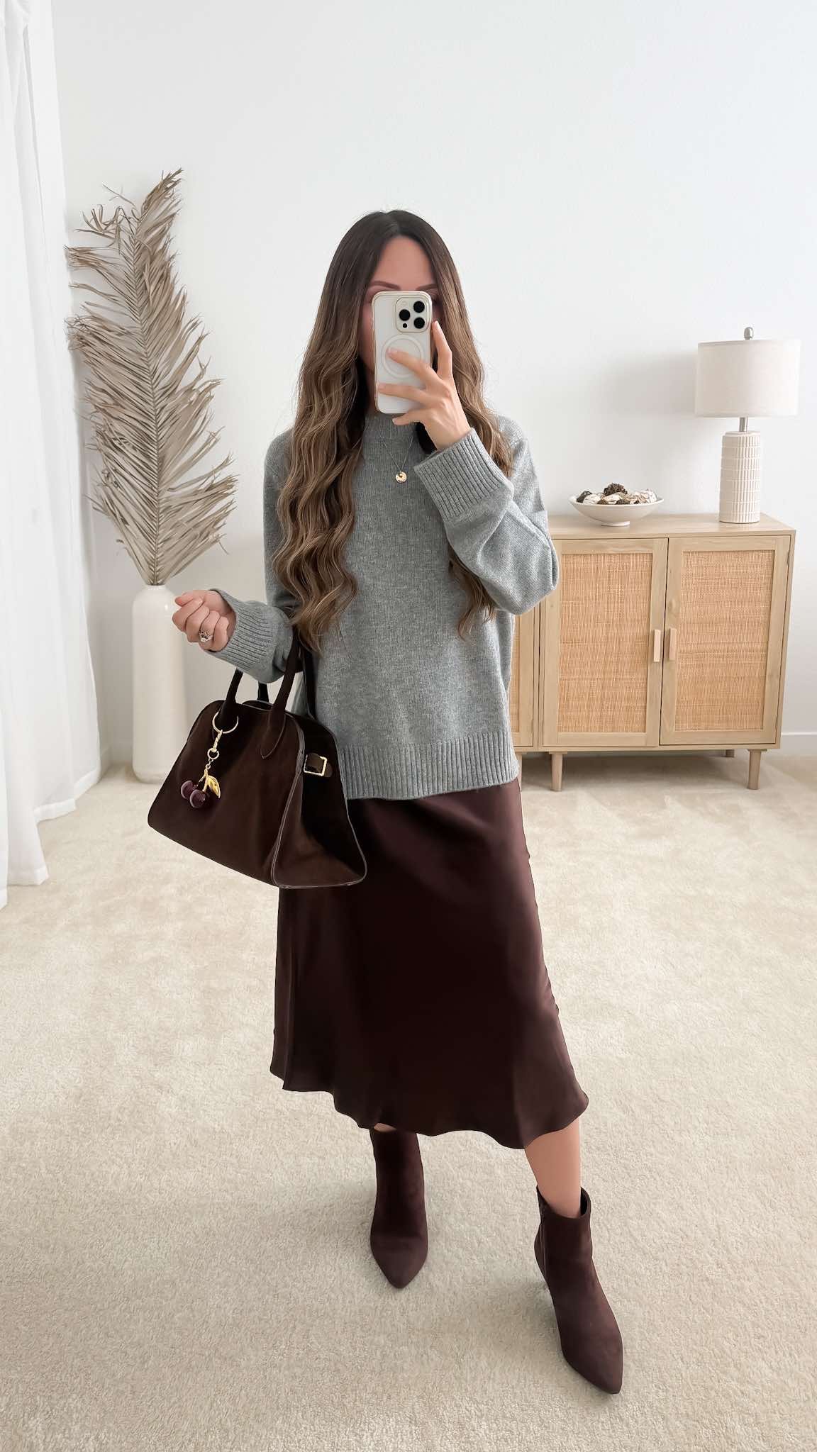Chic fall date night outfit styled with a grey sweater over a chocolate brown silk midi skirt, brown ankle boots, and a brown suede tote bag
