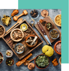 Assortment of spices, herbs, and dried ingredients in bowls and containers on a textured surface.