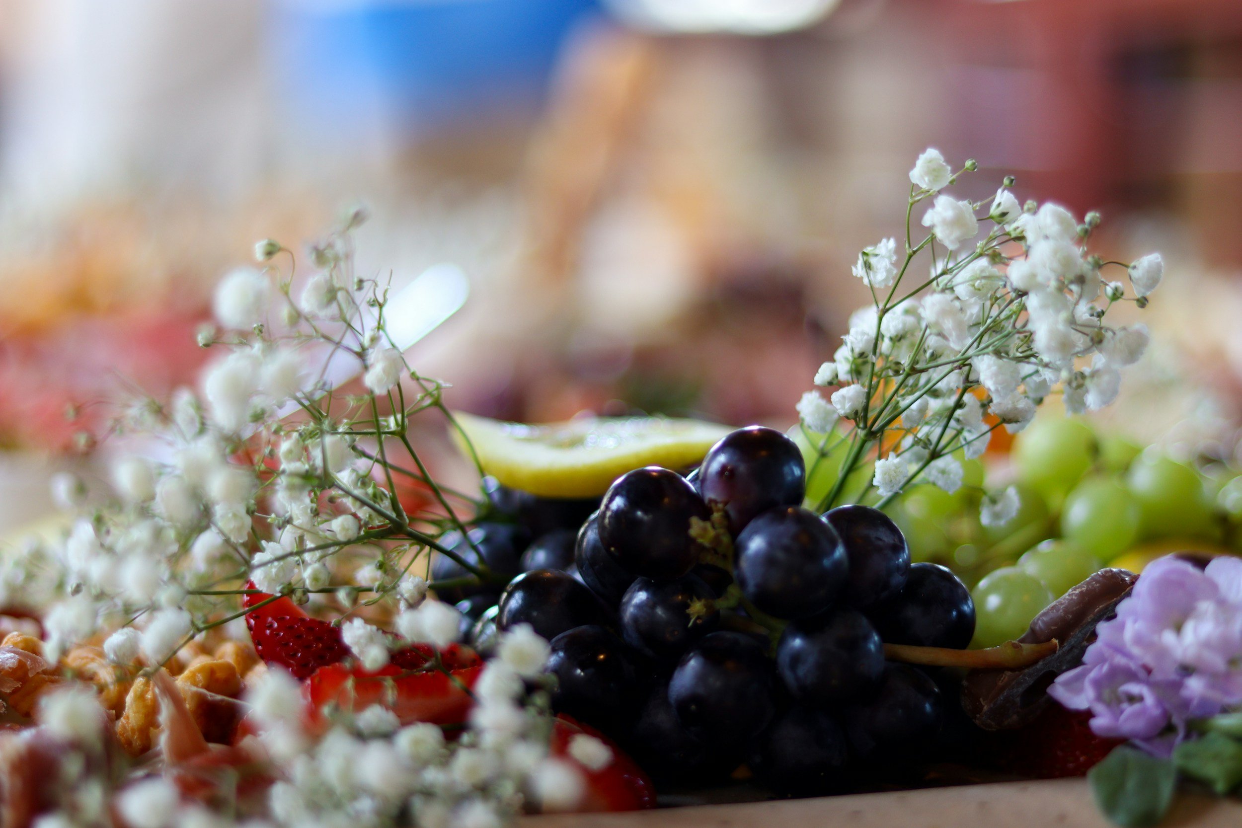 A close-up of a colorful assortment of grapes, strawberries, flowers, and a lemon wedge.
