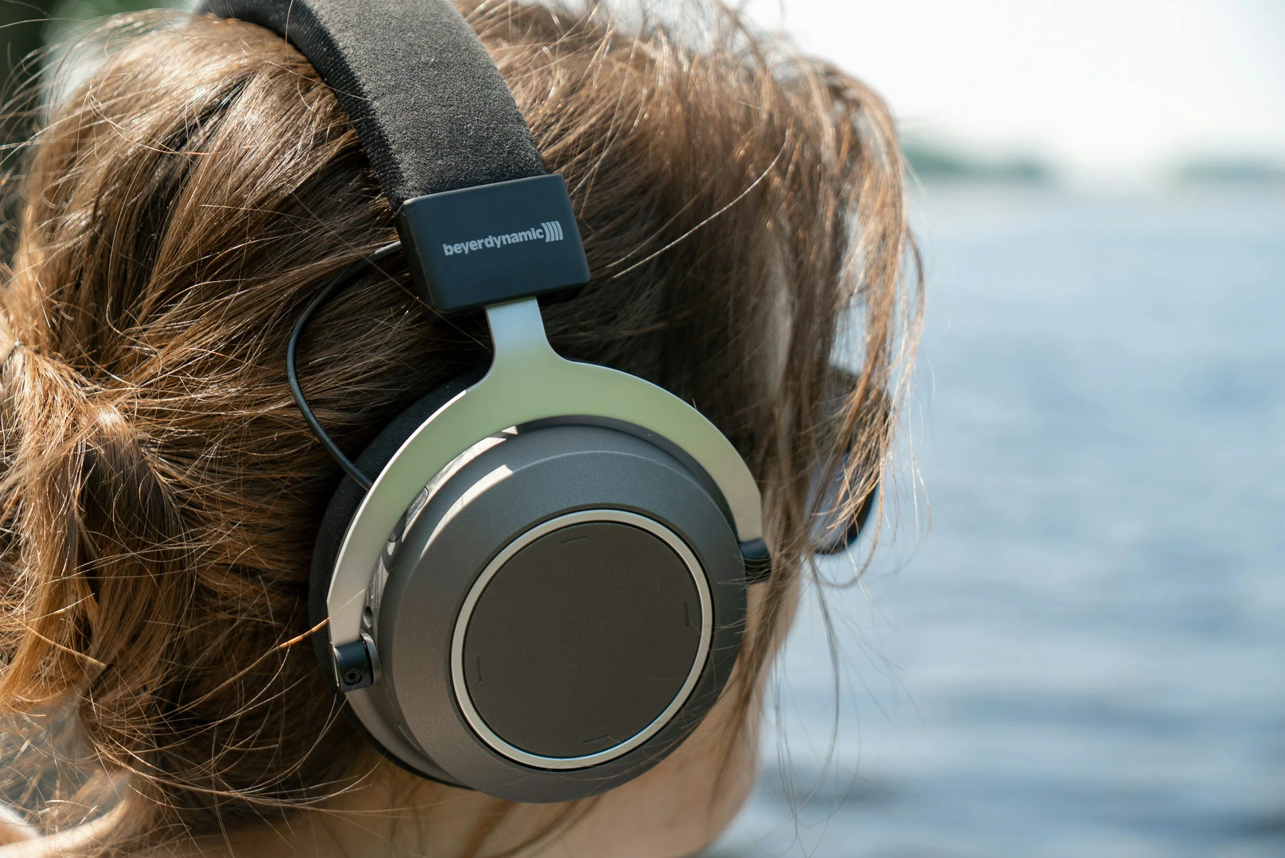 Person with brown hair wearing black headphones near water.