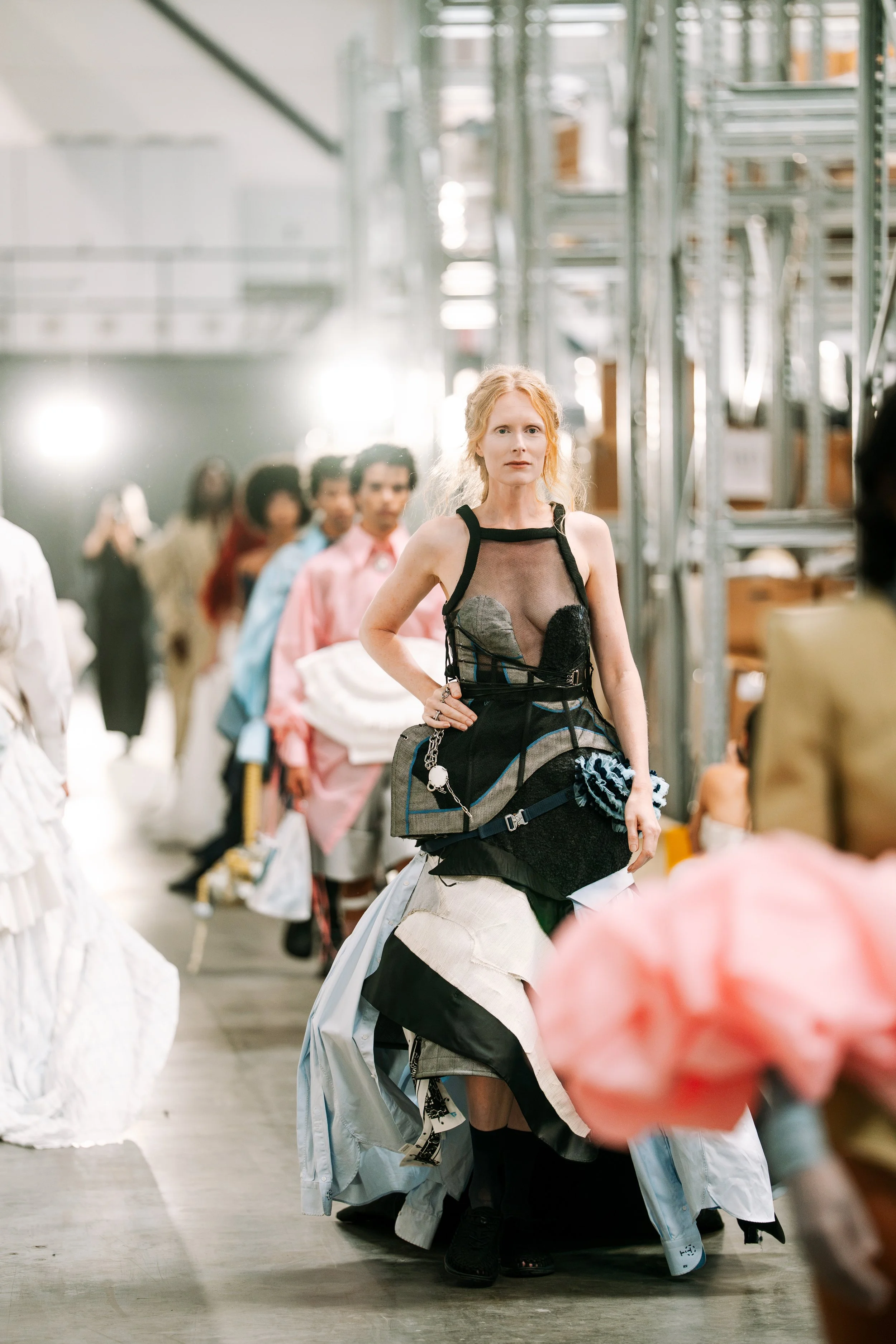A woman with red hair walking on a runway during fashion week. Wearing a corset dress by Tess van Zalinge, all curated by Evy Cornelie, Dirkje Lemmink, and Simone van Ommen. Actress, writer & creative developer Jolanda van den Berg.