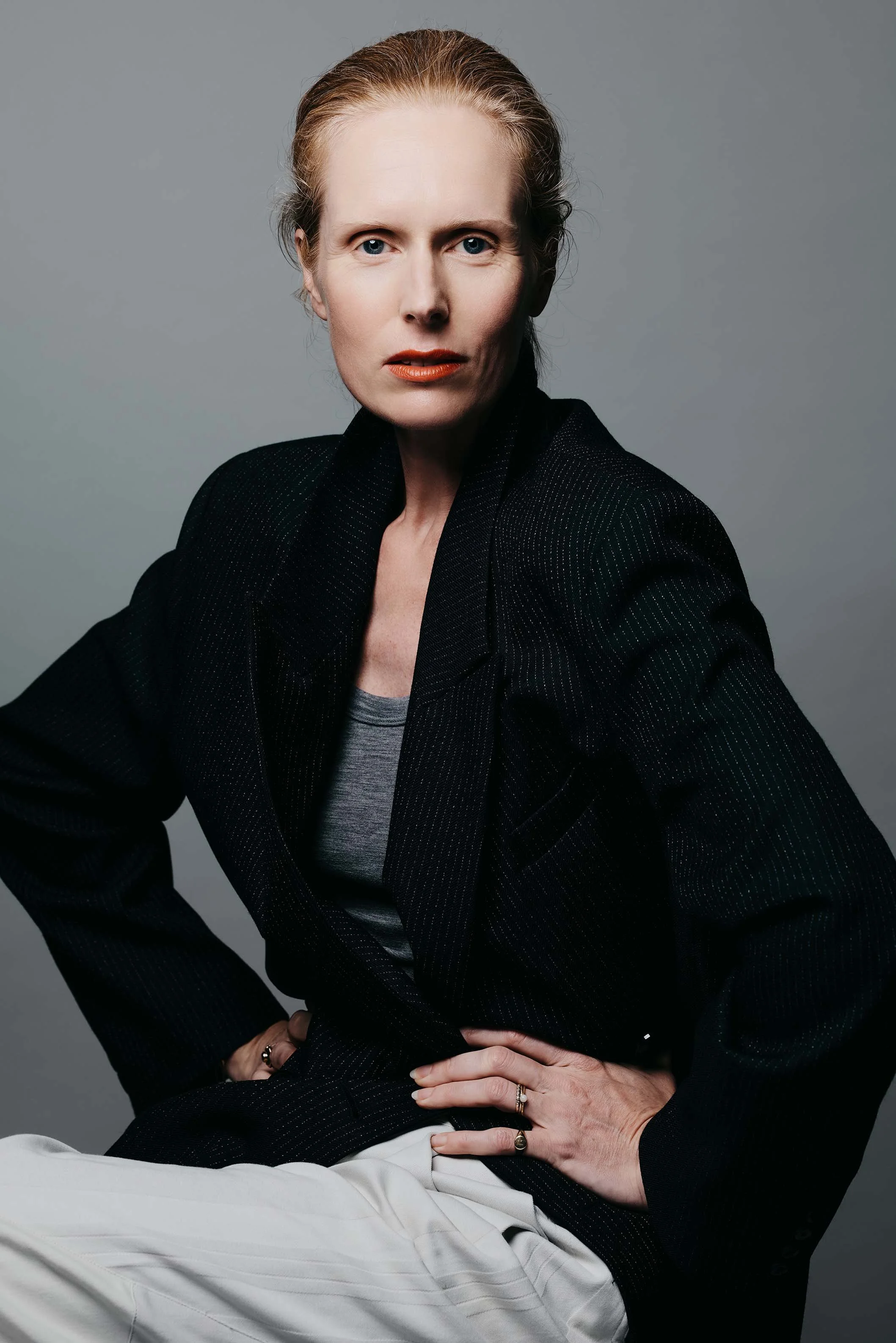 Professional headshot of Jolanda van den Berg, actress, wearing a black pinstriped blazer by Dutch brand Róhe against a gray background. Photo credit: Anne van Zantwijk.