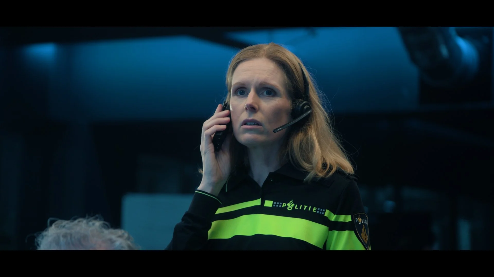 Clip from the Netflix original movie IHostage. A female Dutch police officer wearing a black and yellow uniform with a headset talking on the phone. All rights reserved Netflix. Actress Jolanda van den Berg as Karina.