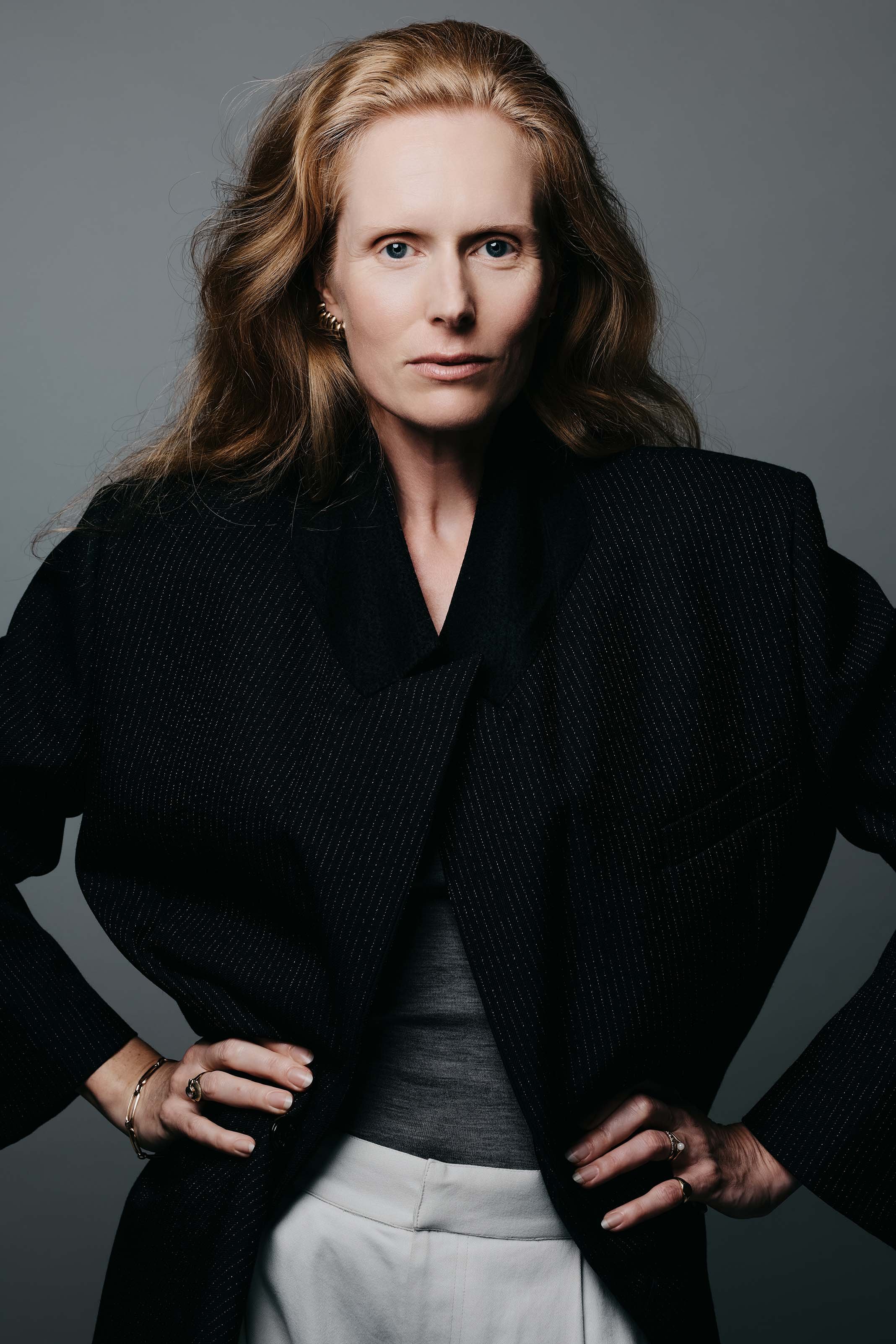 Professional headshot of Jolanda van den Berg, actress, wearing a black pinstriped blazer by Dutch brand Róhe against a gray background. Photo credit: Anne van Zantwijk.