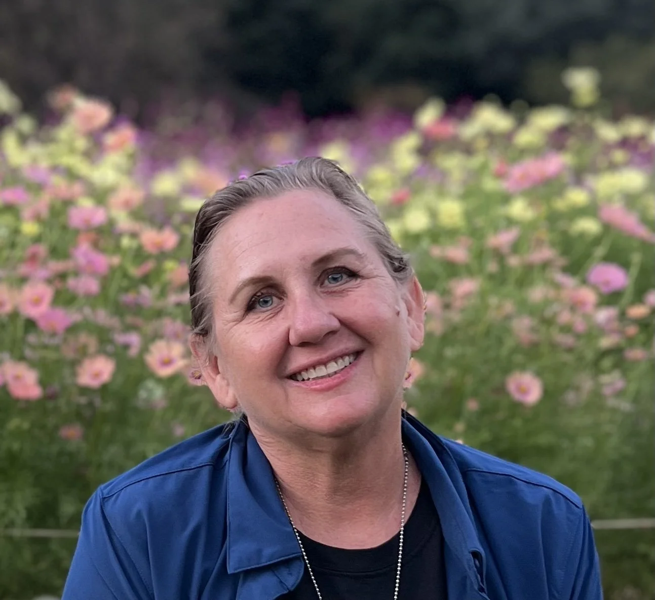 Mel is smiling wearing an dark blue shirt with pink and yellow flowers in the background