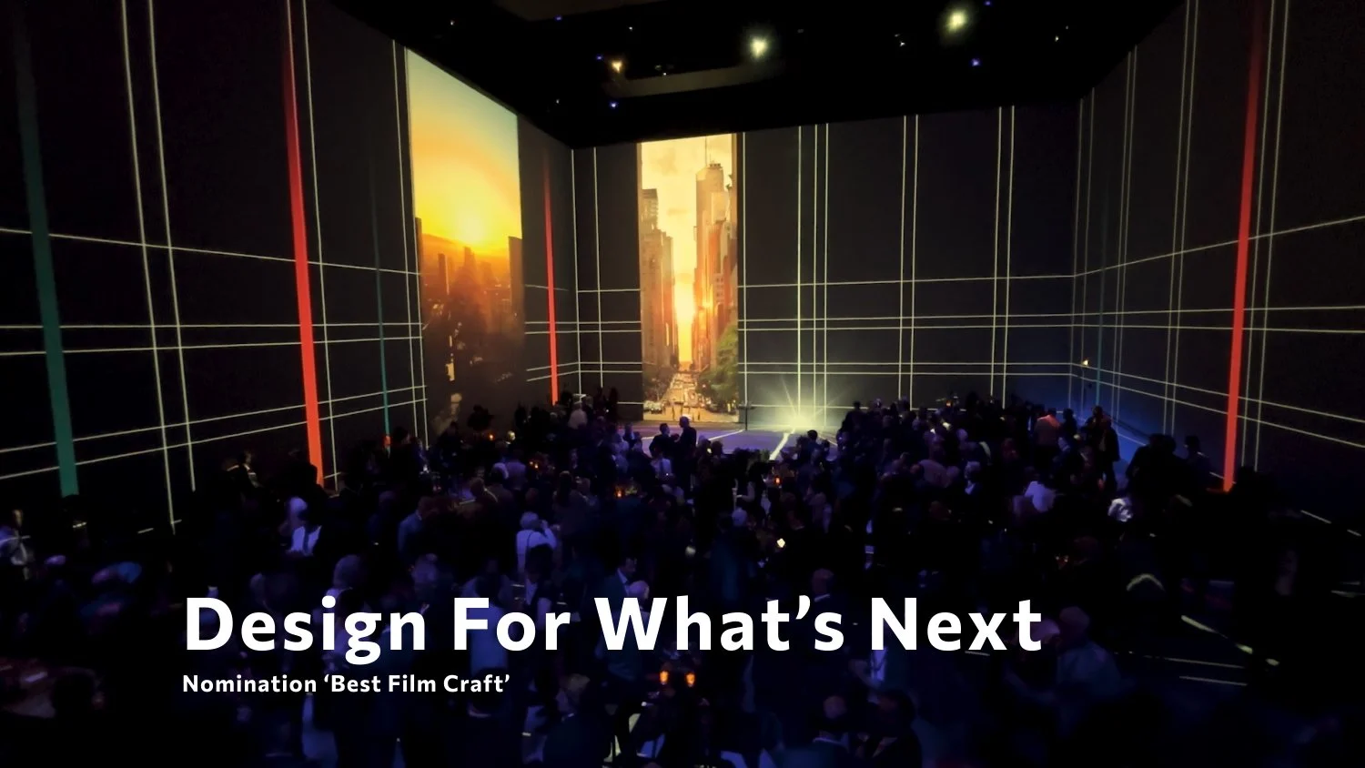 A dark conference room with a large audience watching a presentation screen showing a cityscape at sunset. The screen is divided into three vertical panels with a glowing city at sunset. The text overlay reads 'Design For What's Next' and 'Nomination