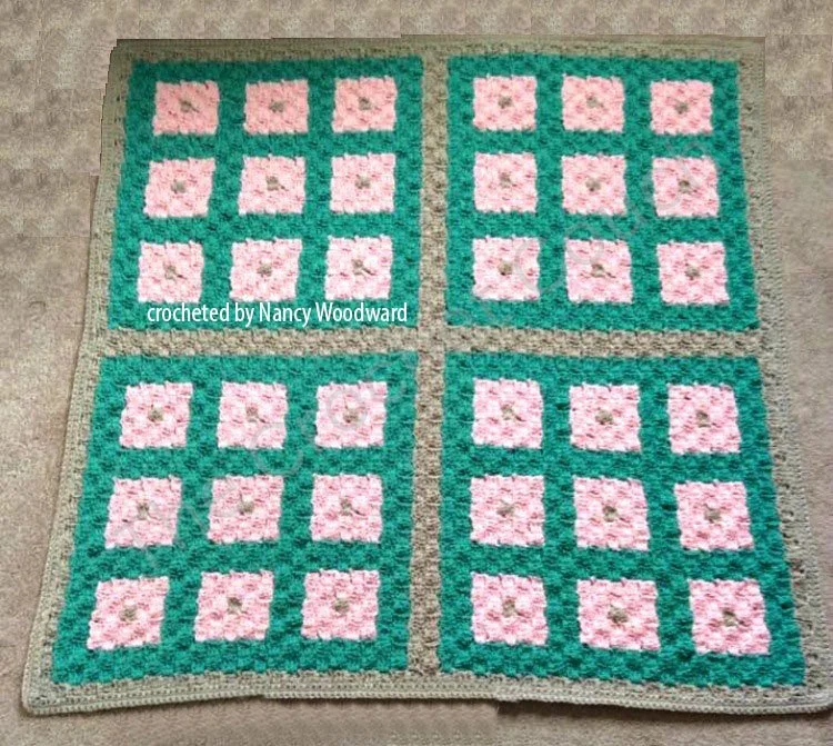 A crochet afghan featuring a patchwork quilt-inspired design in pink and green squares, displayed flat. Ideal for cribs, lap blankets, or decorative wall art.