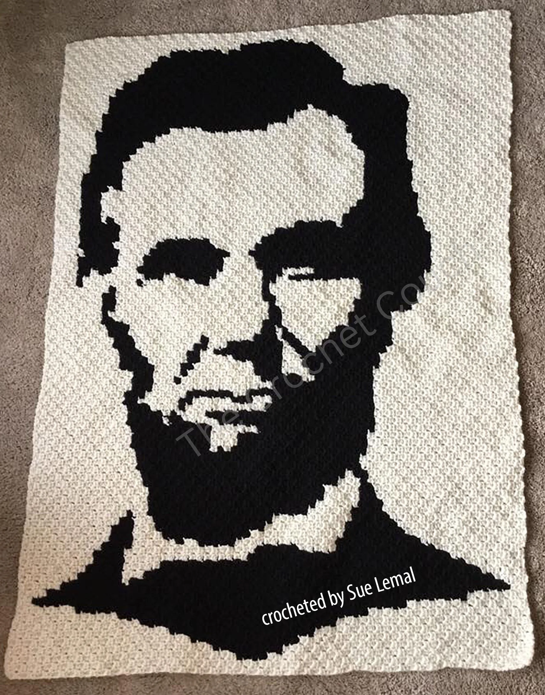 A handmade crocheted afghan featuring a bold black silhouette of Abraham Lincoln on a cream background, showcasing intricate detail and craftsmanship.