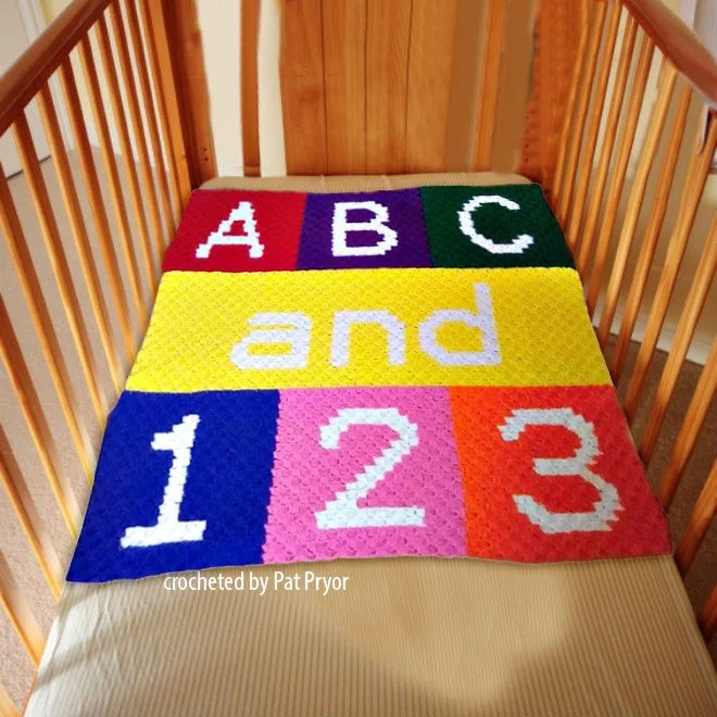 A colorful crochet baby blanket laid across a crib mattress