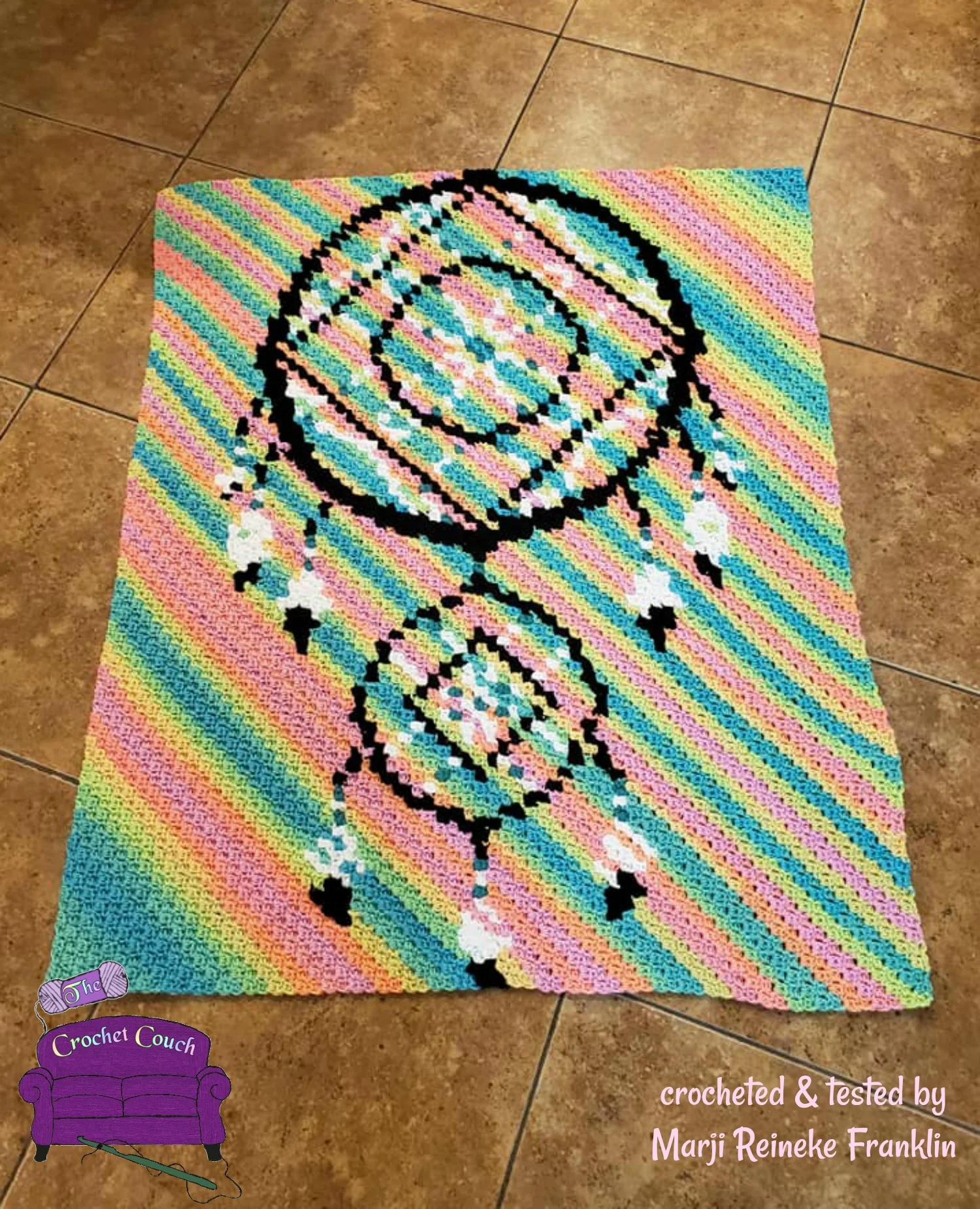 A colorful handmade crochet afghan featuring a black and white dreamcatcher design on a pastel rainbow-striped background.