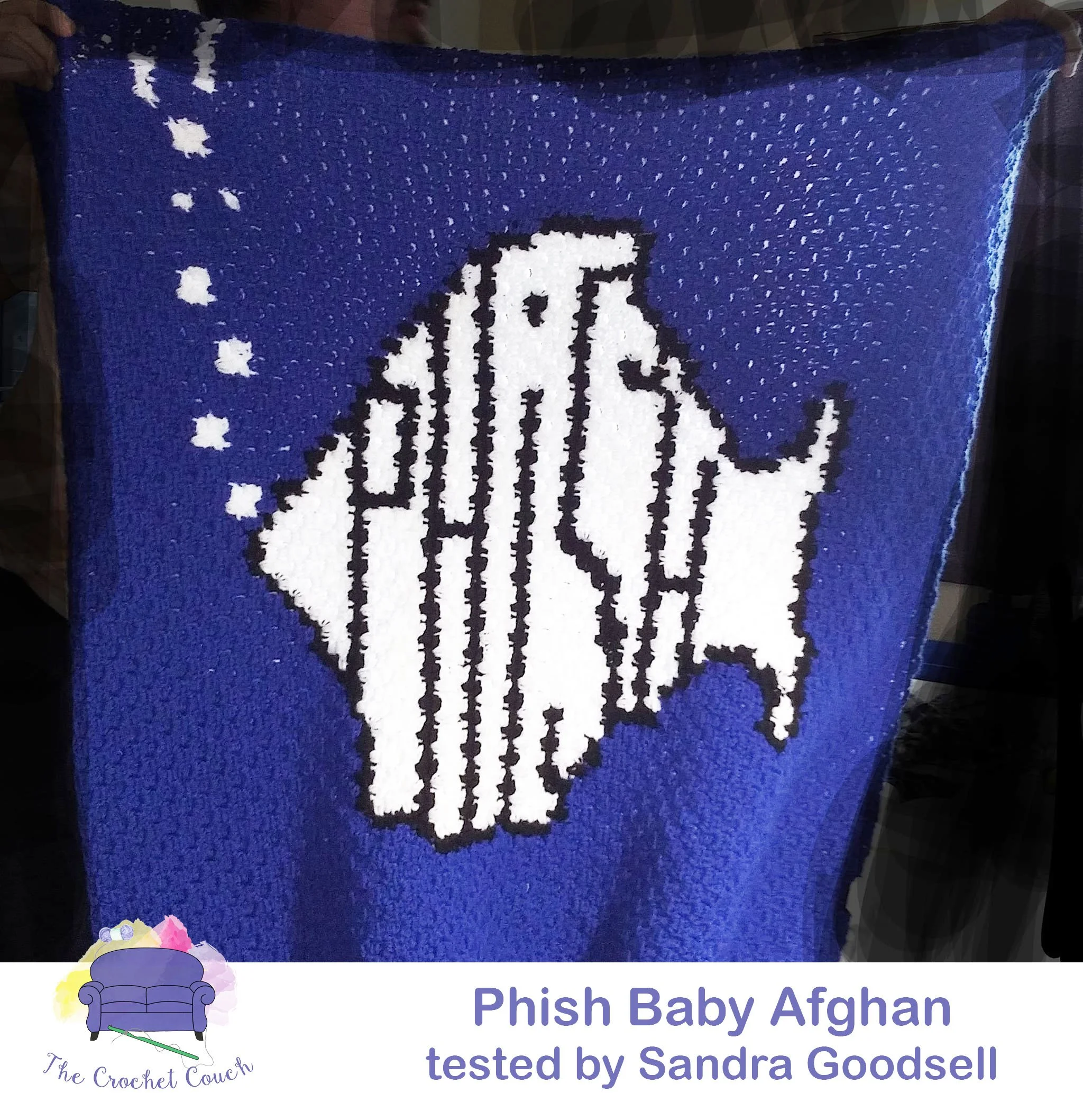 A crocheted afghan featuring a bold white fish silhouette with black outlines, set against a deep blue background