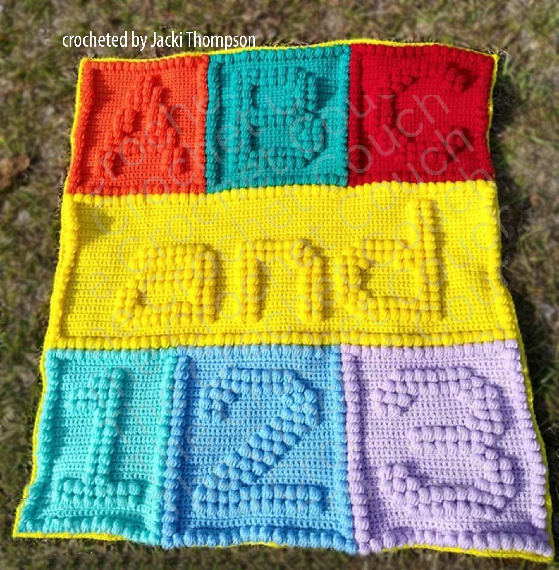 Handmade baby afghan featuring "ABC" and "123" in Bobble stitch on colorful squares of red, teal, orange, yellow, blue, and lavender, displayed on grass.