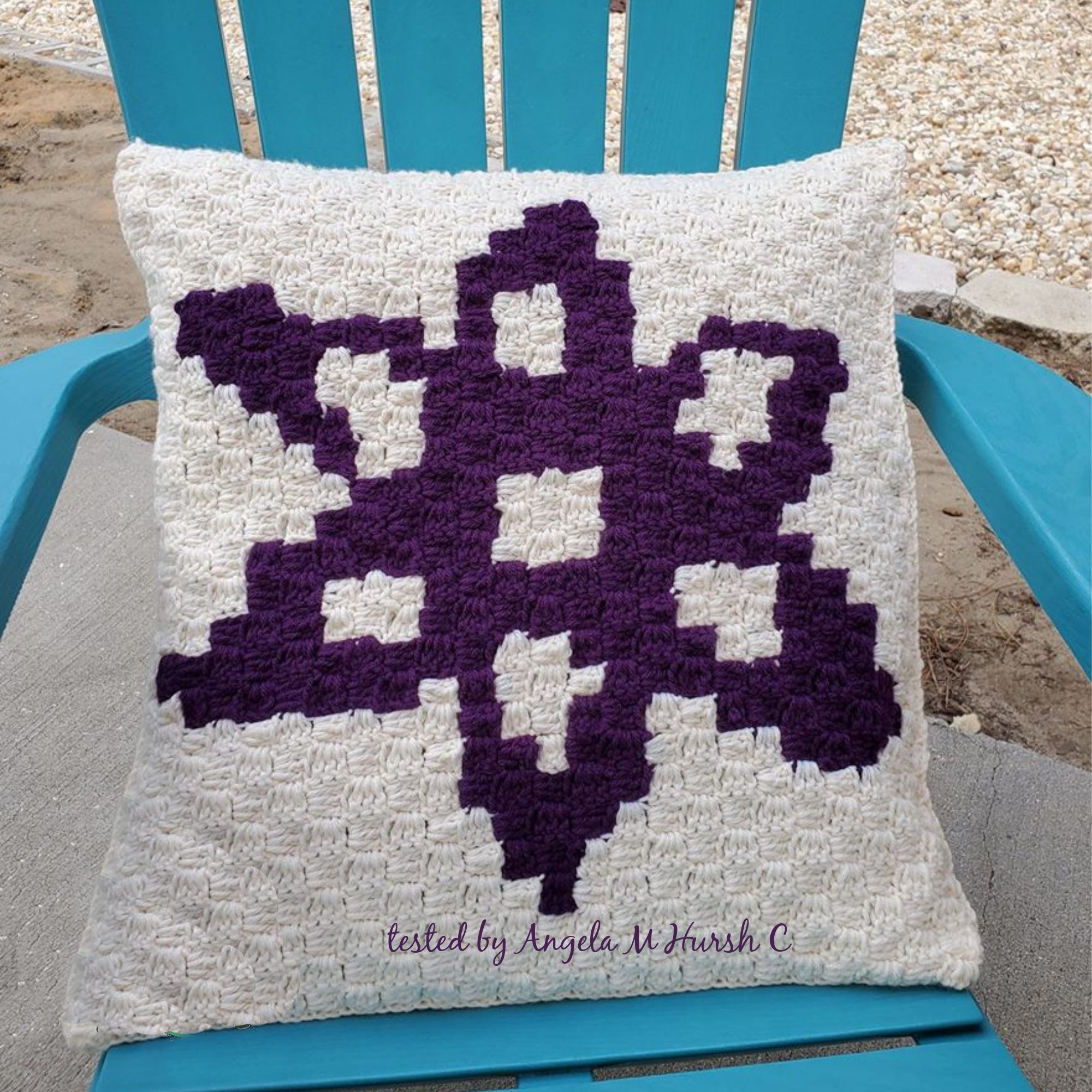 Photo shows a crocheted pillow on a blue adirondack chair.  Pillow has a beige background and a purple design.  Pillow was crocheted by Angela M. Hursh