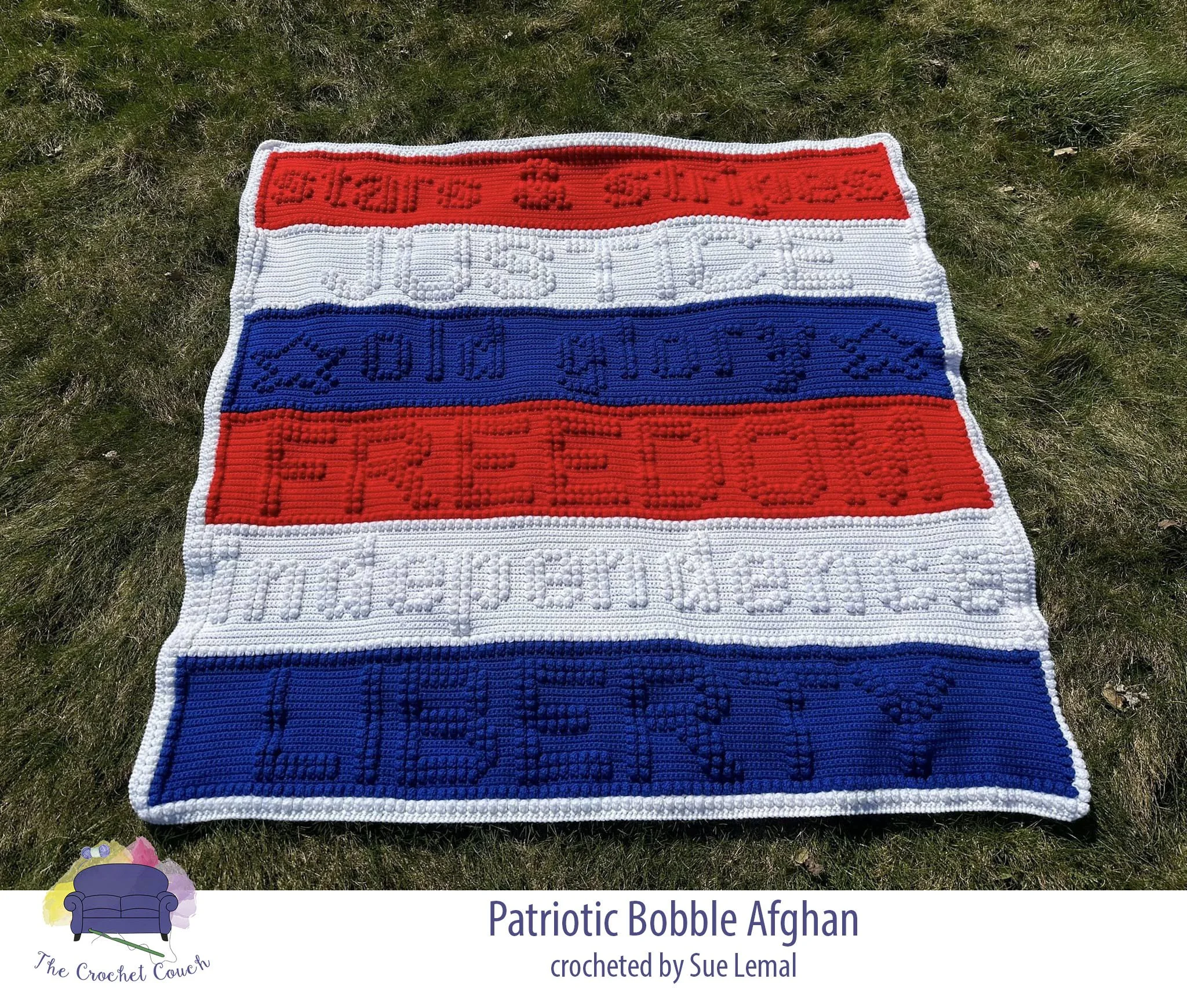 Crocheted afghan shown laid outside on grass - afghan is red, white and blue with a patriotic theme and includes words:  independence, justice, old glory, liberty, stars & stripes, freedom.