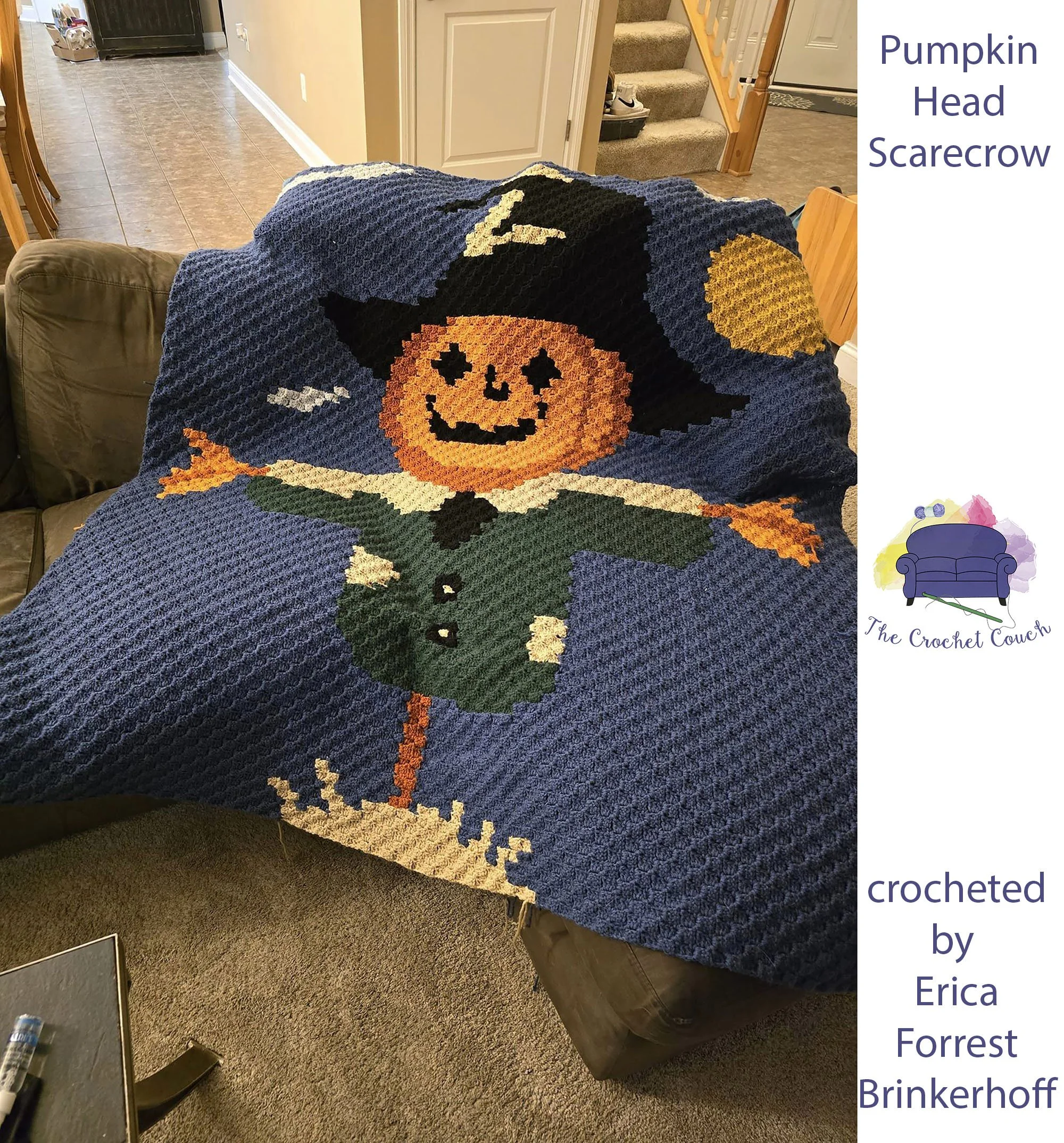 Crocheted afghan is shown draped over a couch - it depicts a pumpkin head scarecrow wearing a pilgrim hat.  Background is a twilight blue.