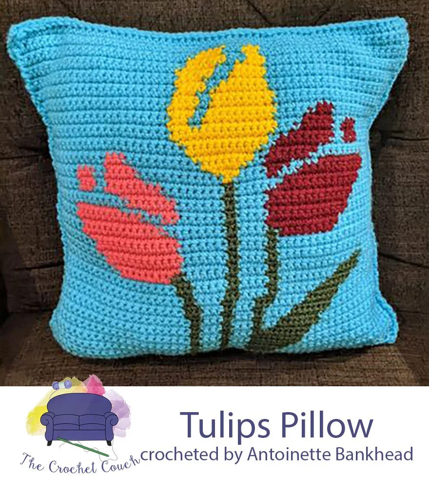 Crocheted pillow done in single crochet has a bright blue background with tulips done in pink, red and yellow.  Tulip pillow crocheted by Antoinette Bankhead