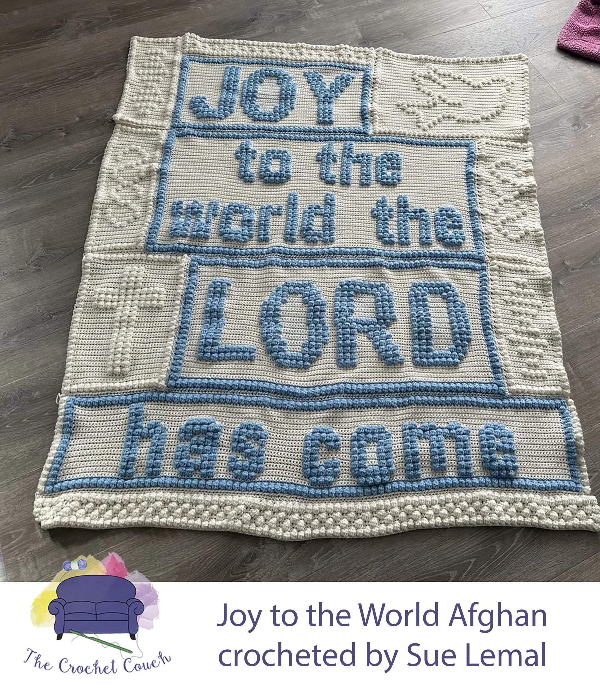 This photo shows a crocheted blanket with the text JOY to the world the LORD has come in blue on a cream background. It has a cross and dove in cream on either side, with intricate stitching