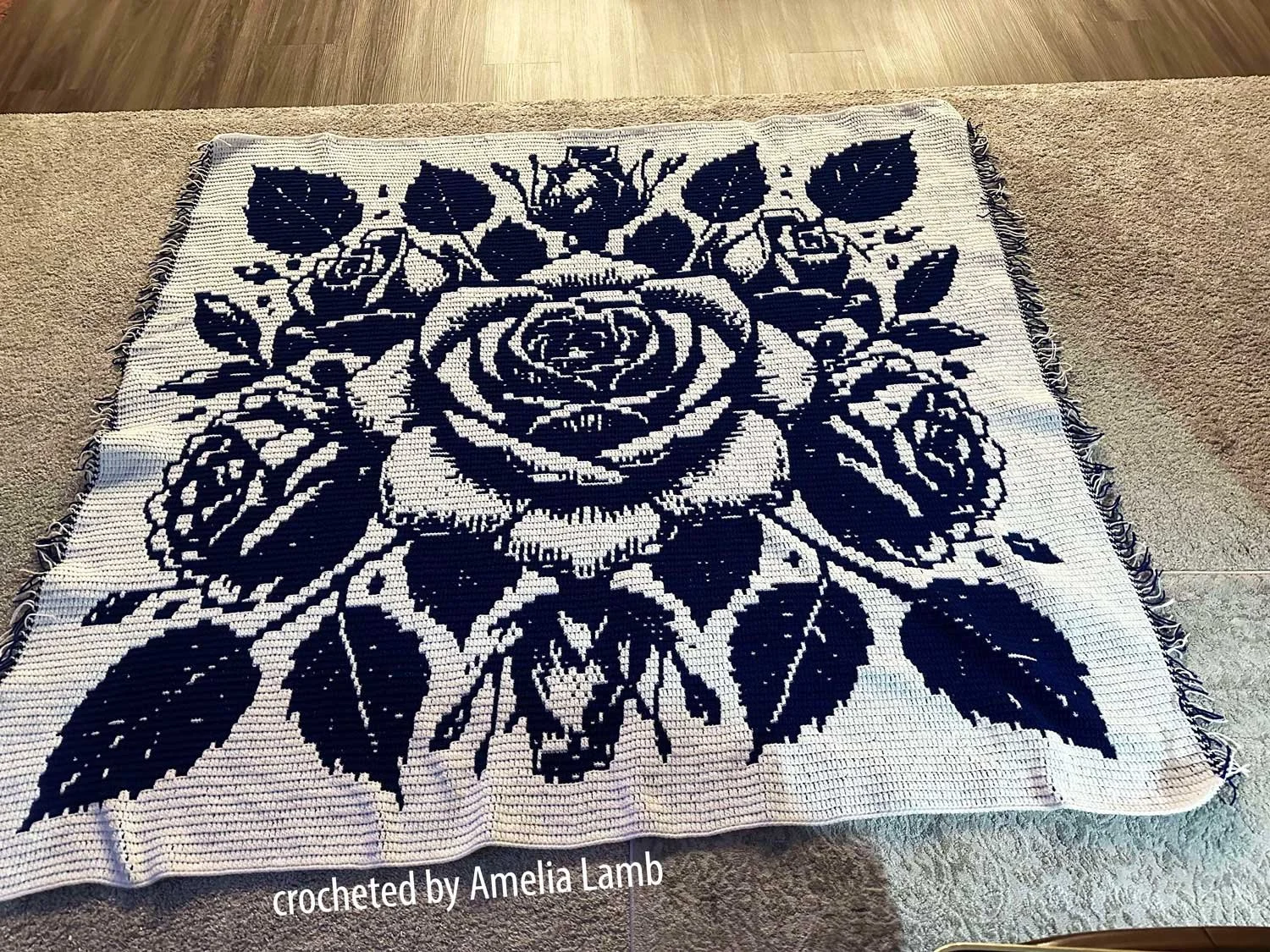 Afghan white background with black roses and leaves, shown laying on floor - crocheted by Amelia Lamb
