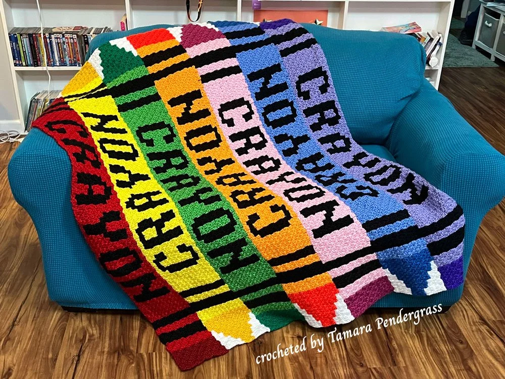A colorful crochet afghan made in a corner-to-corner style, featuring stripes designed to look like large crayons