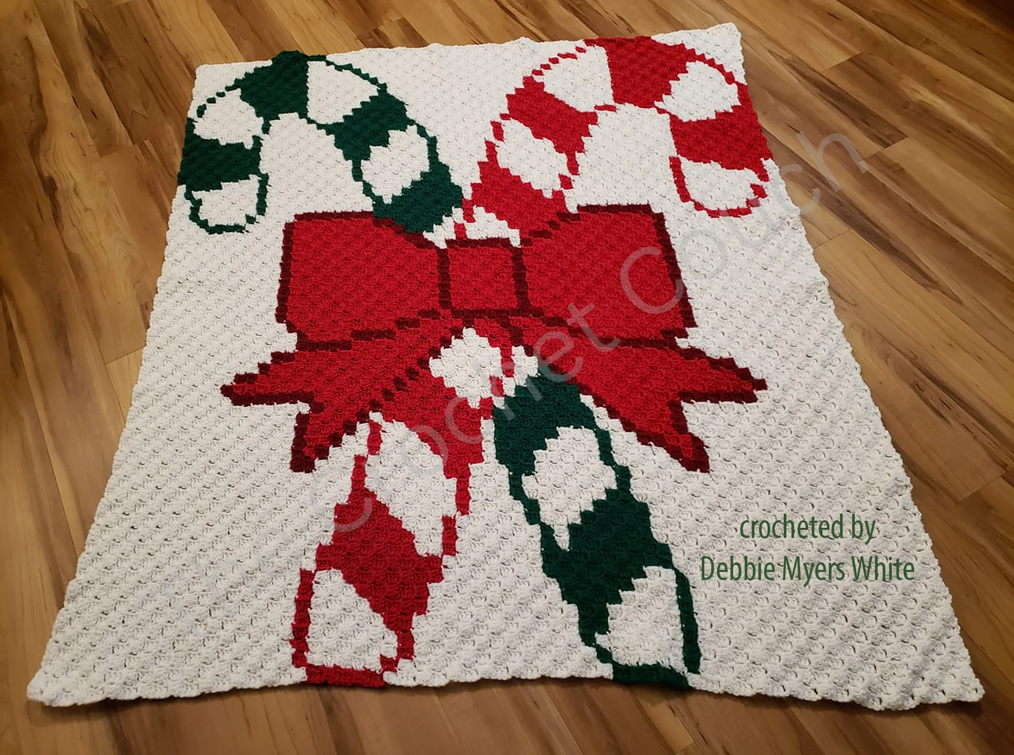 Crochet afghan featuring two candy canes crossed with a red bow on a white background.