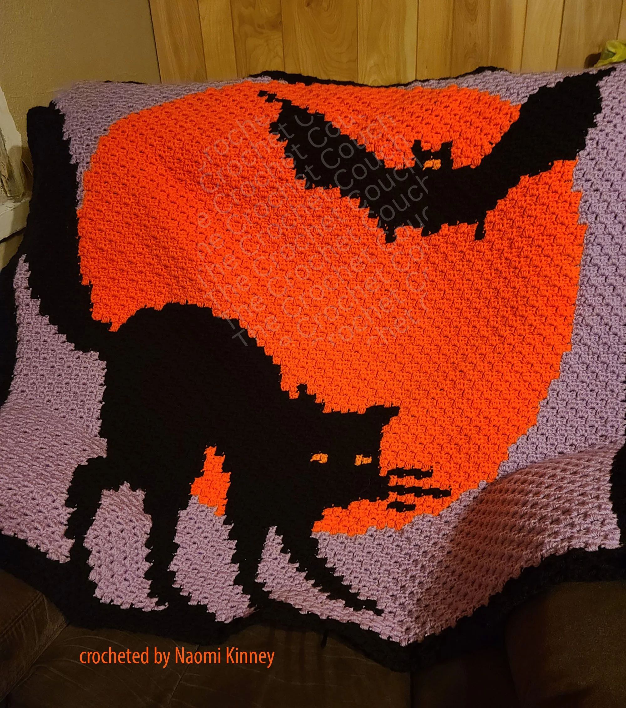 Crocheted Afghan shown laying on couch - depicts a black cat in front of a full moon with bats in the sky.  C2C Afghan crocheted by Naomi Kinney