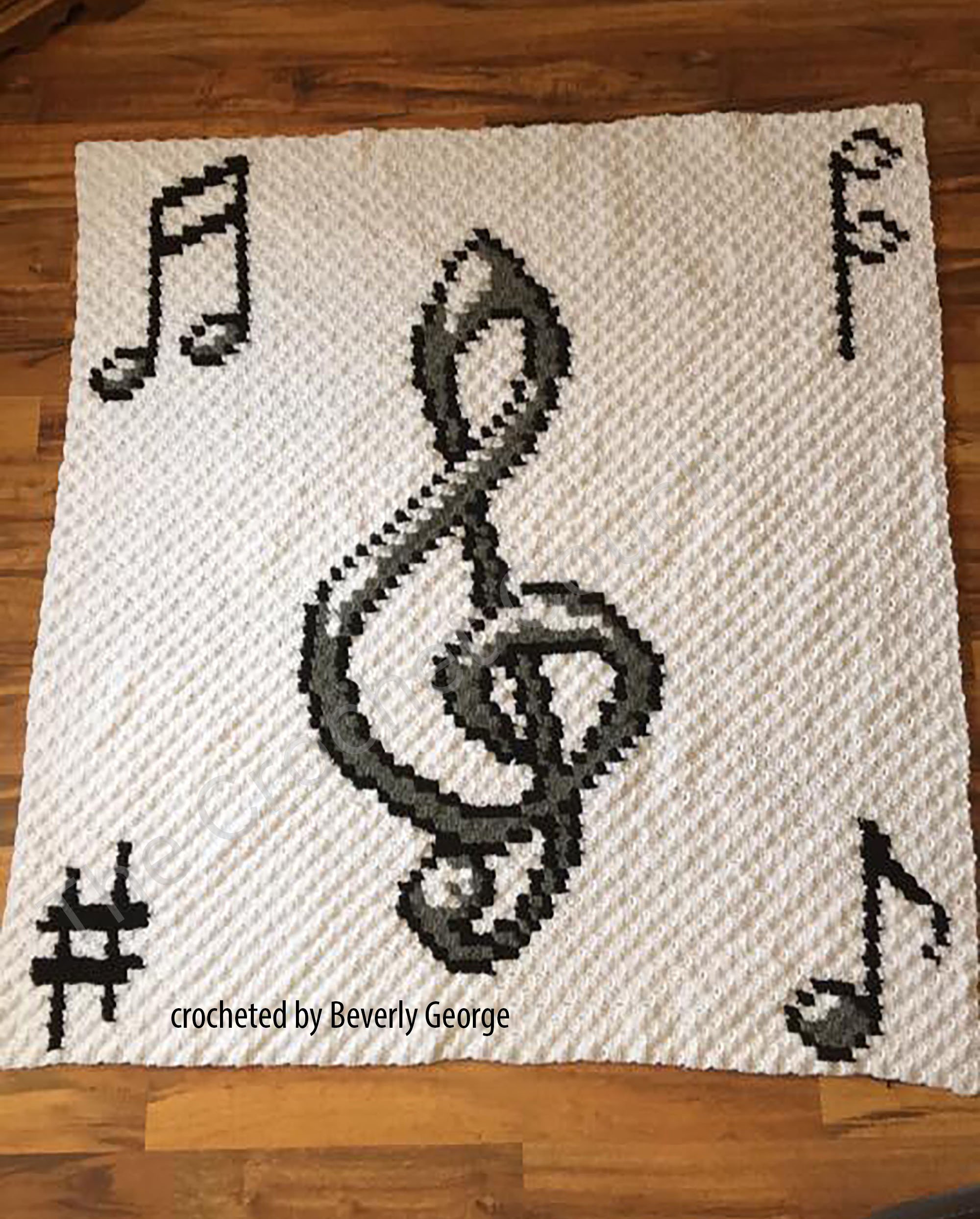 Crochet afghan featuring a large treble clef and musical notes in black against a white background.
