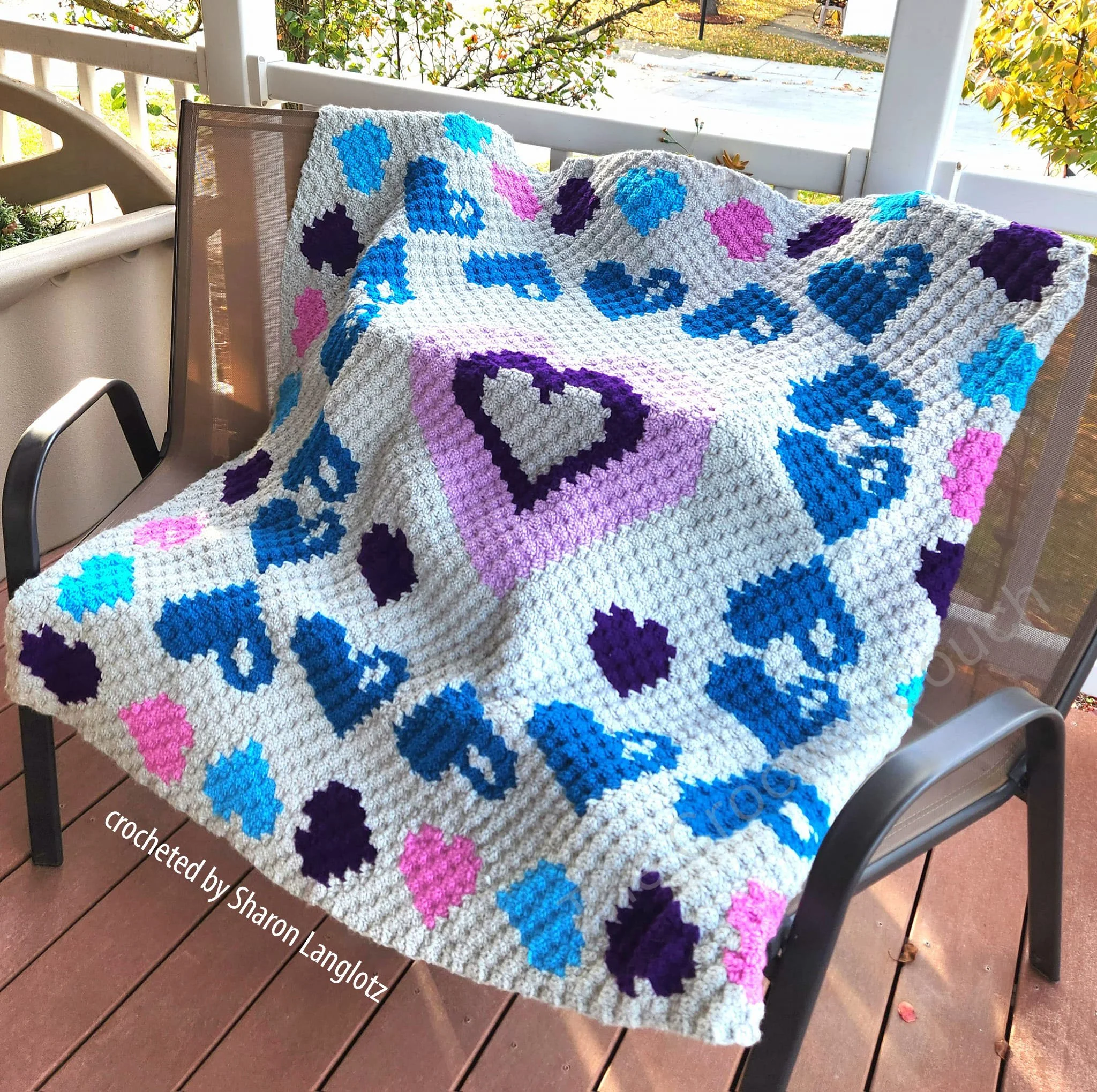 A colorful crochet afghan with a corner-to-corner (C2C) heart-themed design in shades of pink, purple, blue, and white.