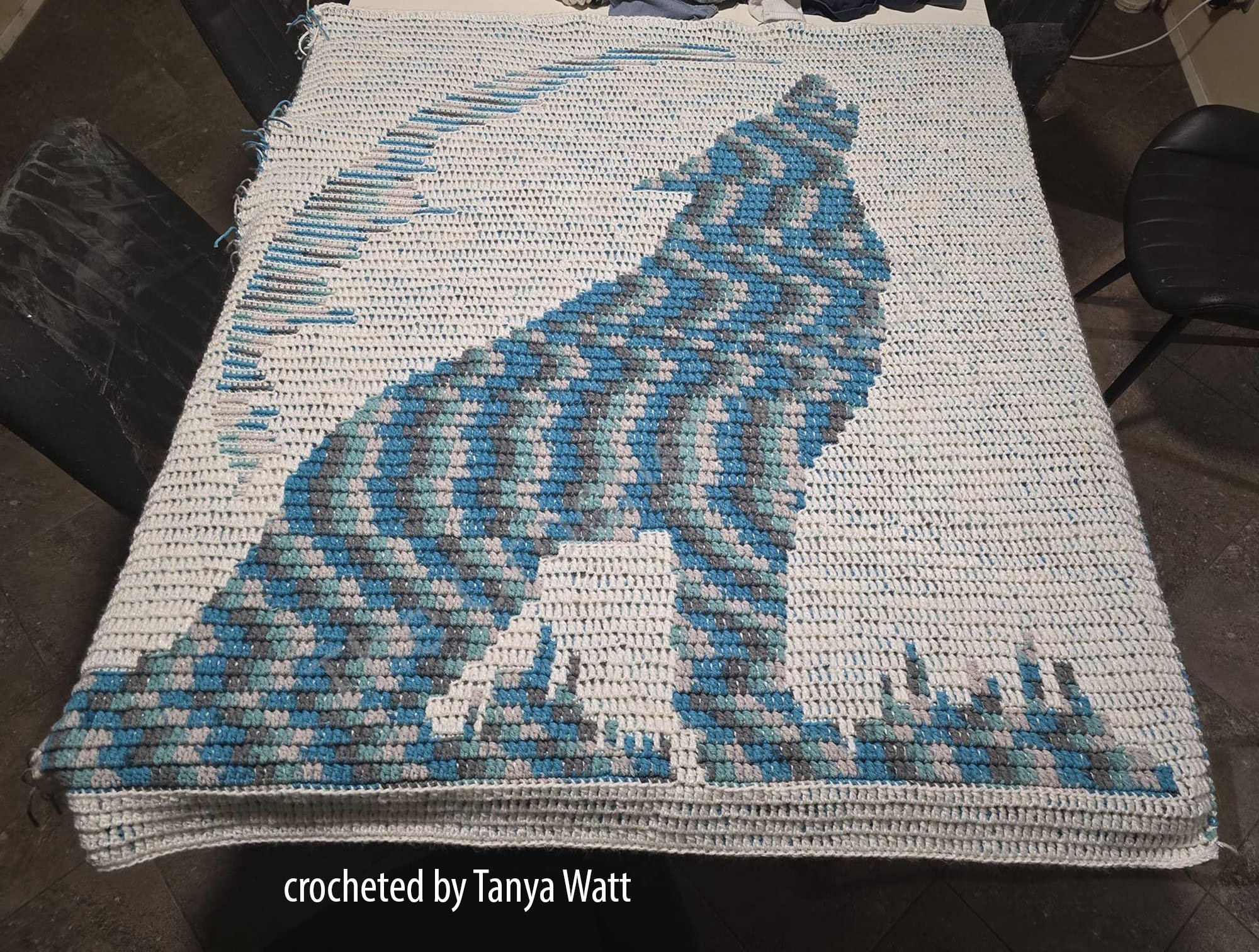 A crocheted baby afghan featuring a detailed howling wolf silhouette in shades of blue and gray