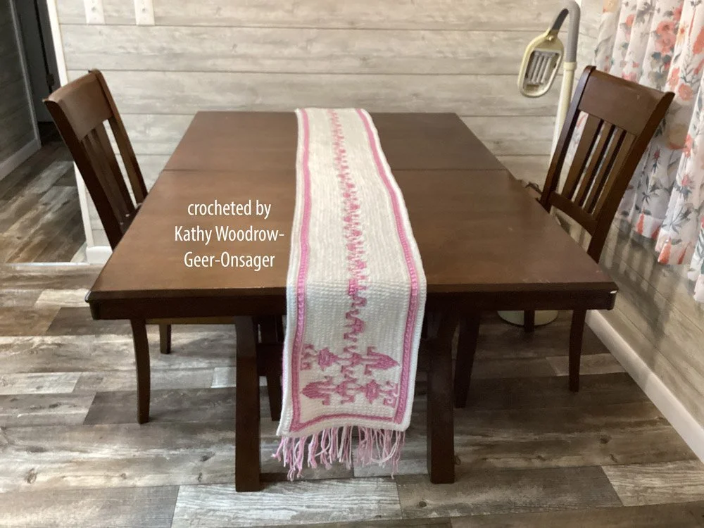 Handmade crochet table runner featuring a central geometric arrow pattern and fringe edges, displayed on dining tables in neutral and pink color schemes.