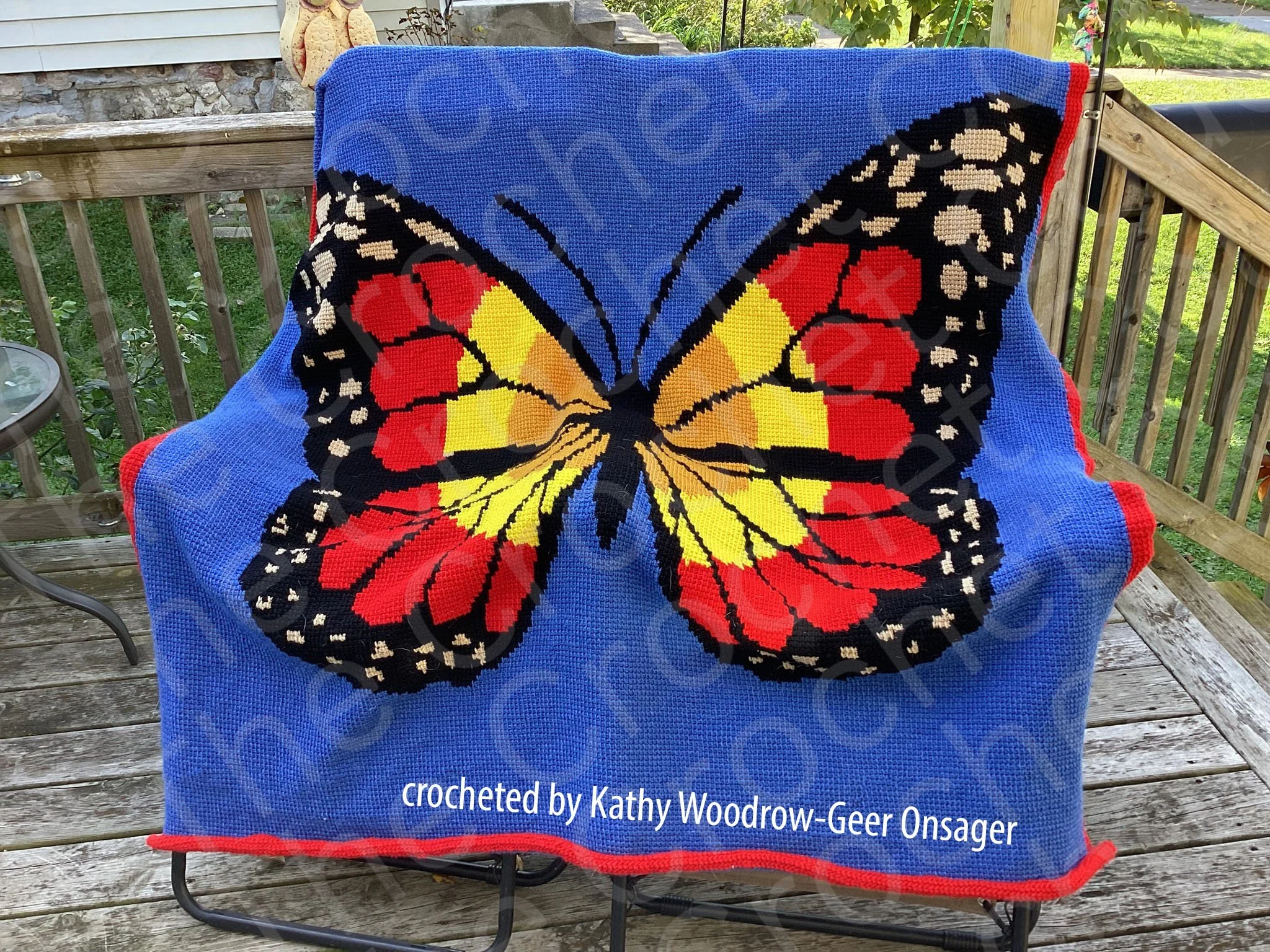 A handmade afghan featuring a large, vibrant butterfly in sunset colors of red, yellow, and orange on a blue background.