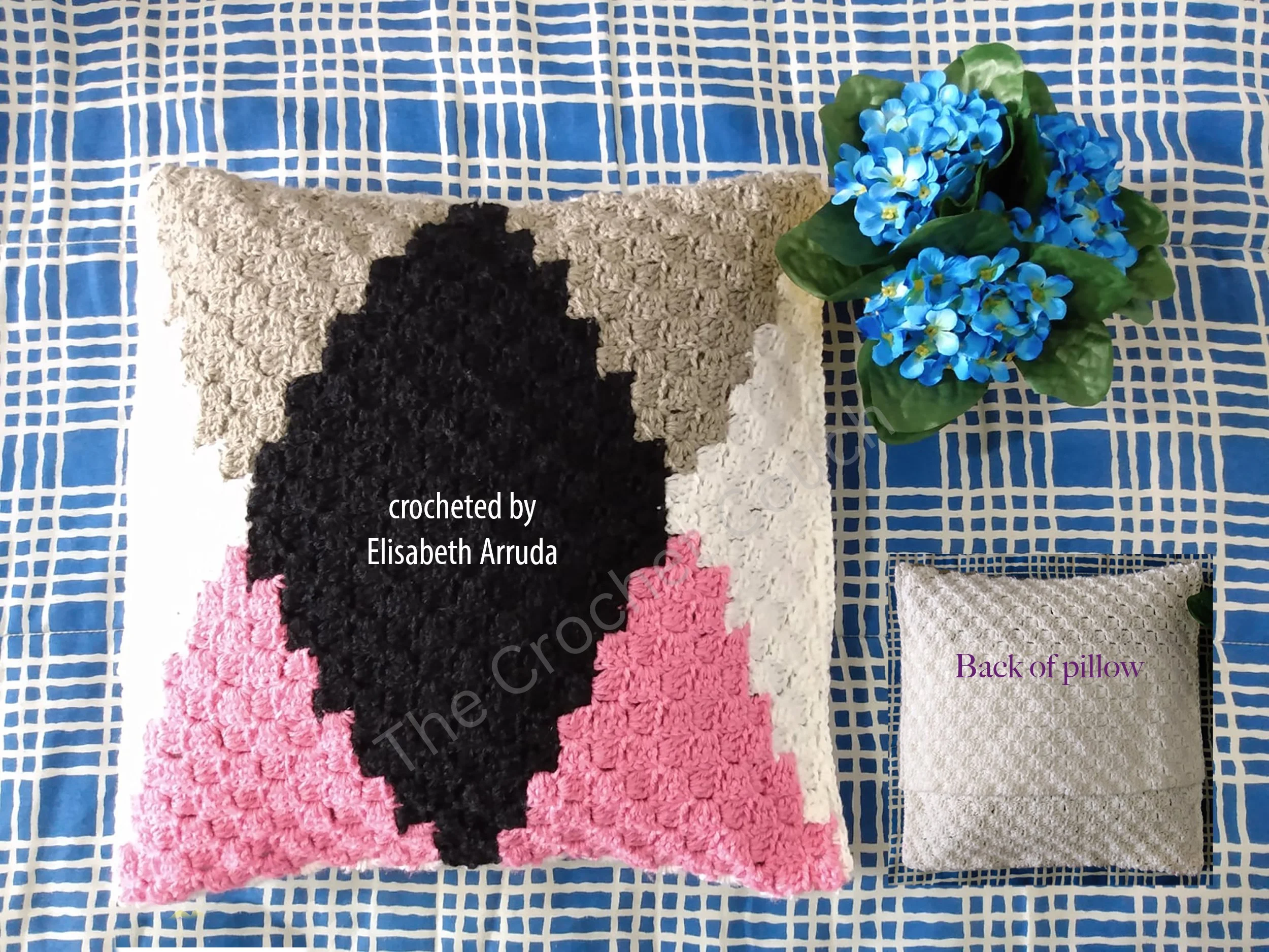 Crochet pillow featuring a black diamond design with beige, white, and pink accents.