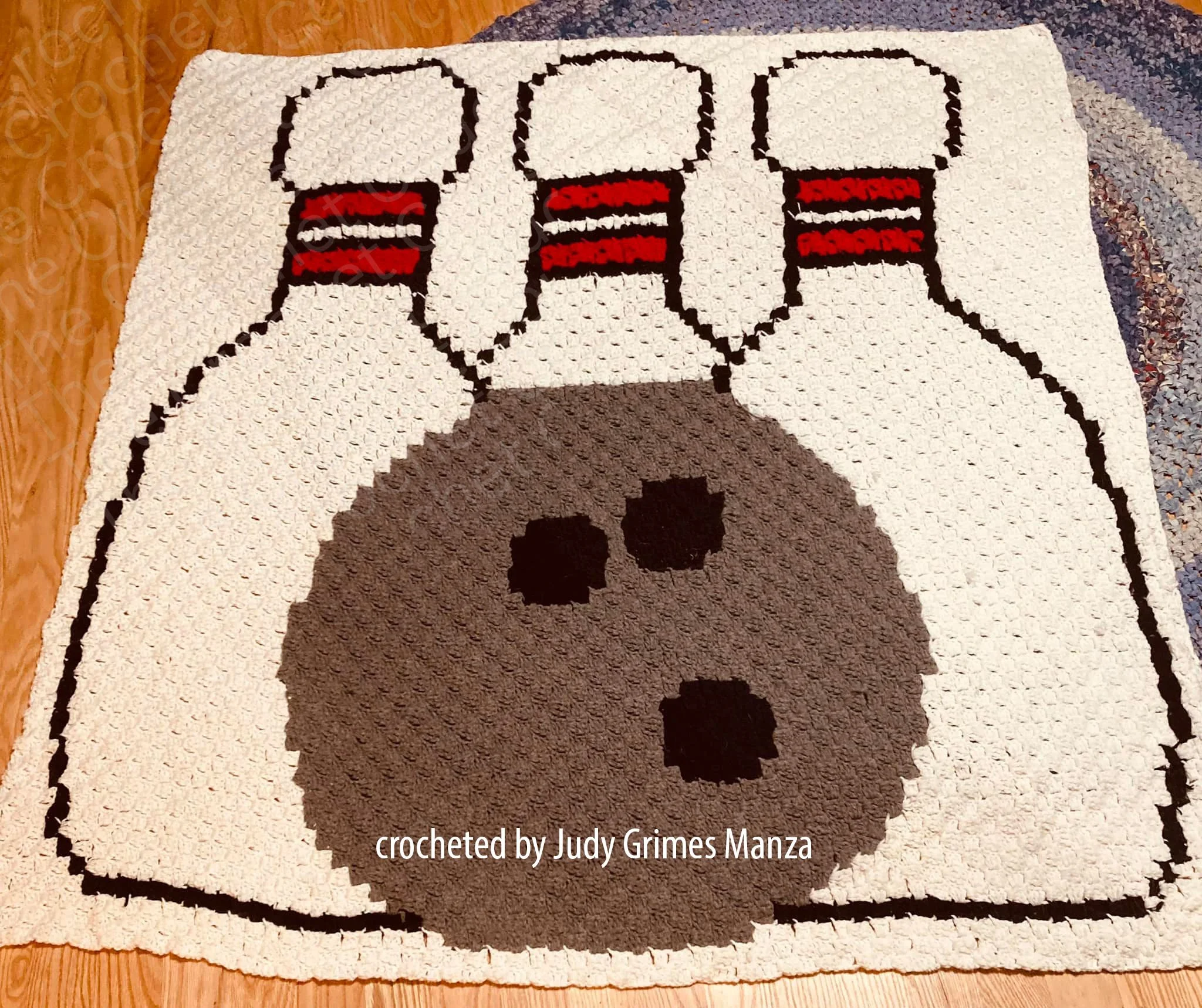 Crochet afghan with a large bowling ball and pins design in grey, black, red, and white colors.