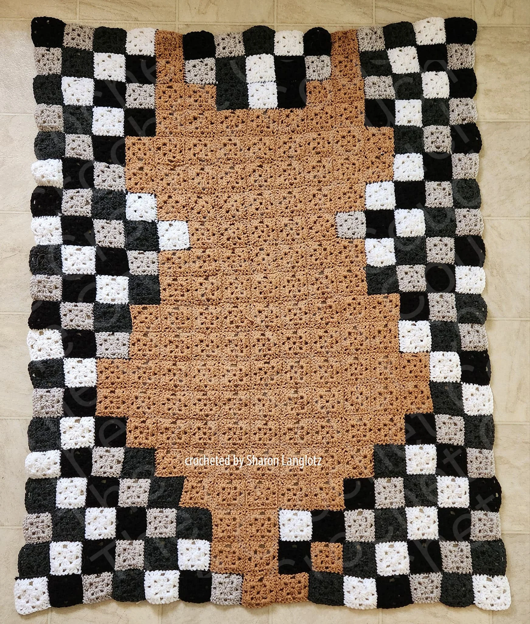 Handmade crochet blanket featuring a cat silhouette in a rustic brown color, created with crocheted granny squares, surrounded by a checkerboard border in black, white, and gray