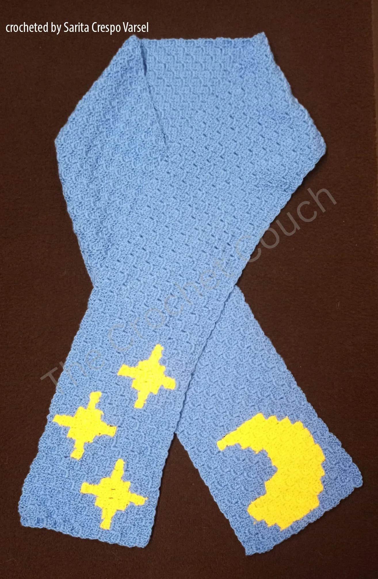 A crochet scarf featuring yellow stars and a crescent moon on a blue background, crocheted in the corner-to-corner (C2C) technique. Crocheted by Sarita Crespo Varsel.