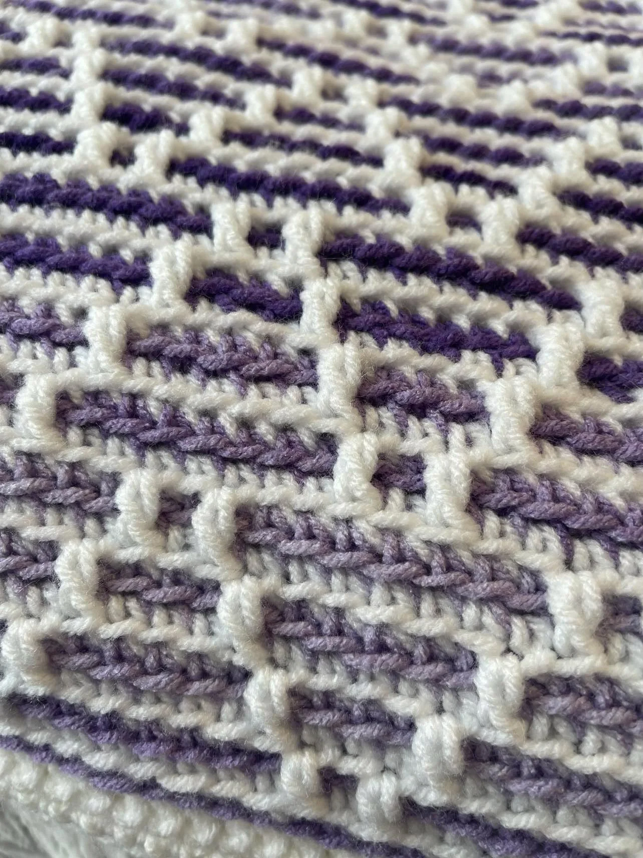 A beautifully textured mosaic crochet baby blanket with a ladder-like geometric design in soft purple and white.