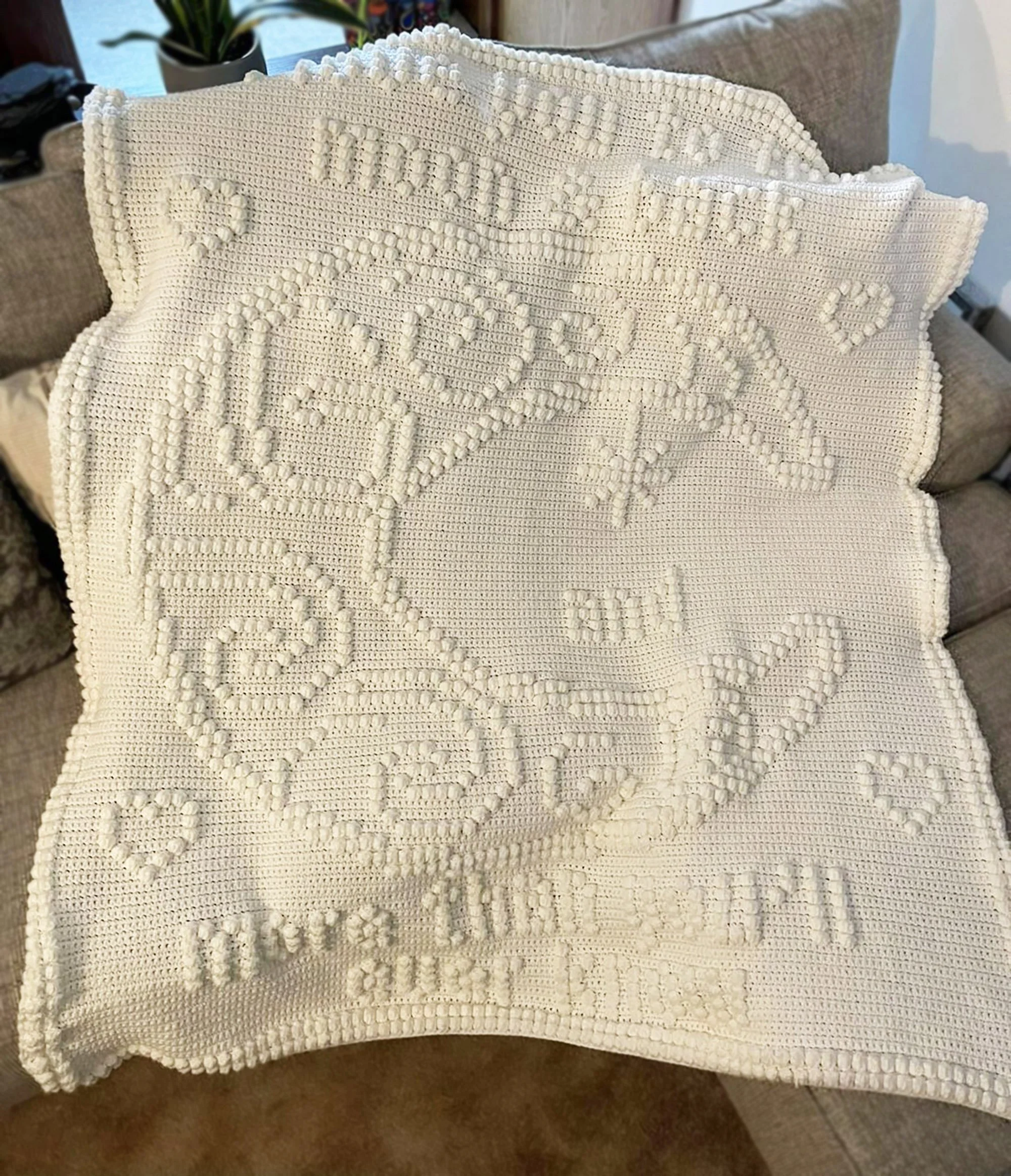 A white crochet afghan with a raised crescent moon and star design, featuring the words 'I love you to the moon and back.' The intricate pattern adds texture and warmth, perfect for a cozy setting