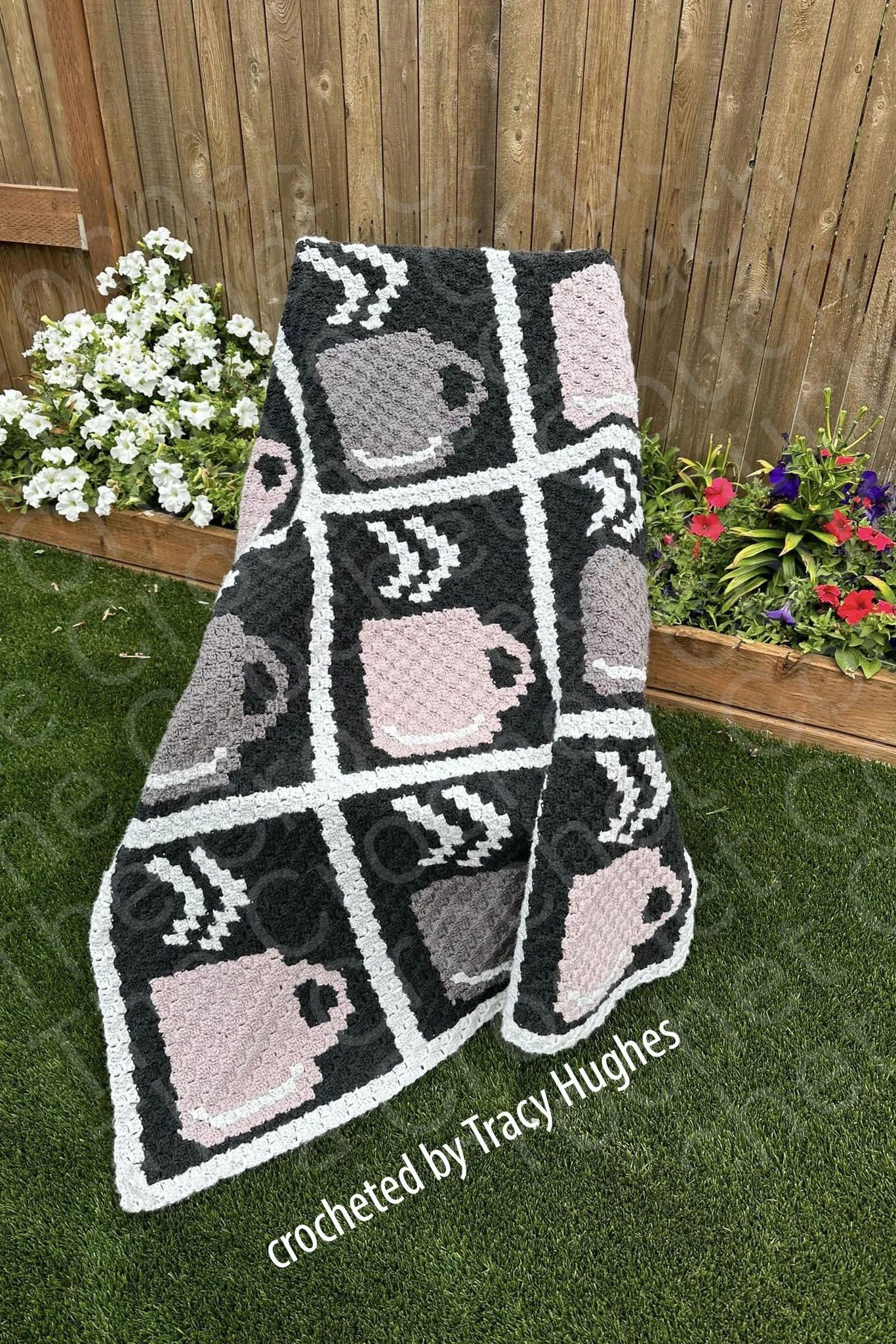 A crochet afghan featuring a grid of nine steaming coffee mugs, with the pattern's original colors being teal and gray. This tester’s version is shown in pastel pink and gray tones.