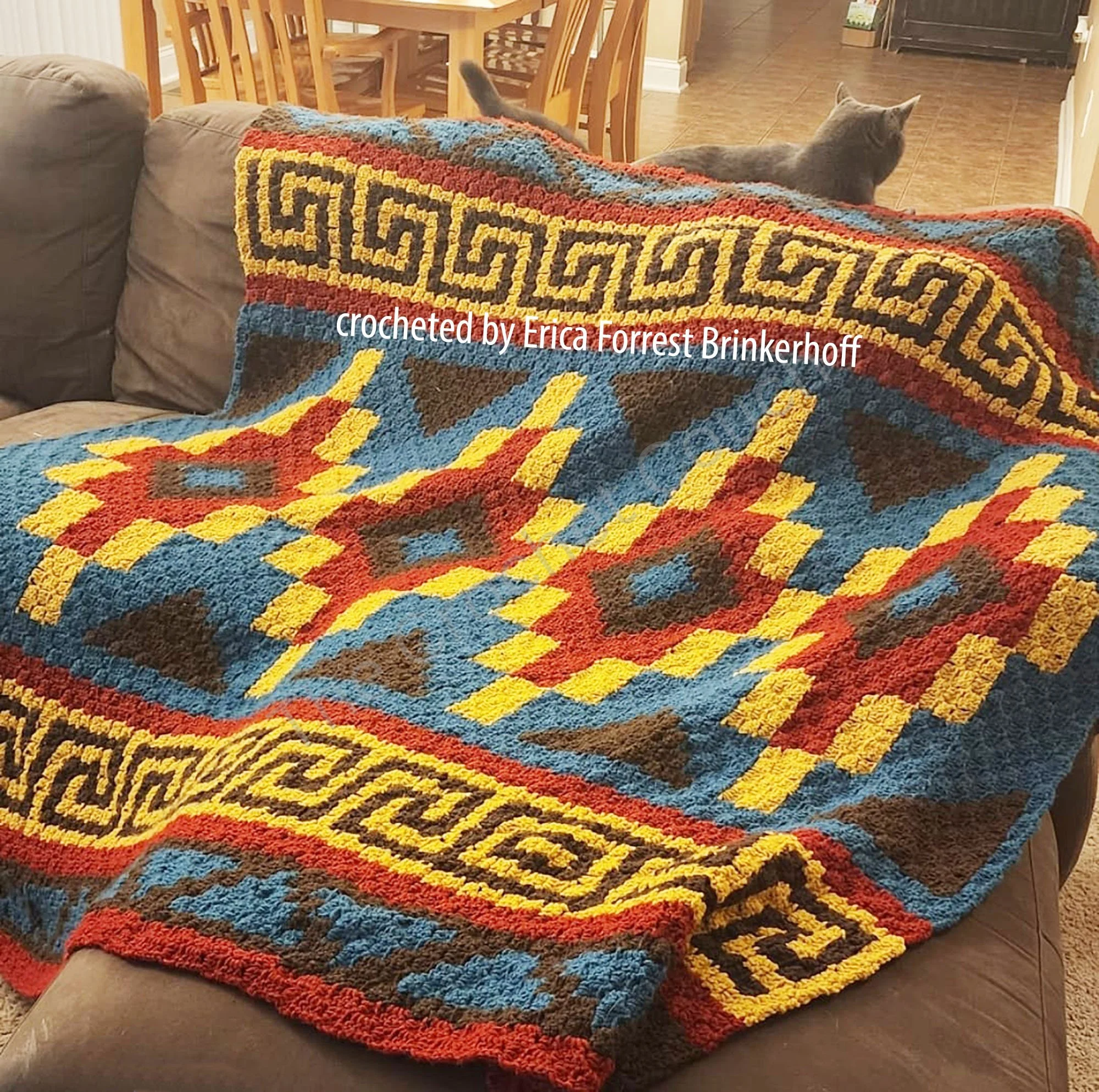 A vibrant crochet afghan featuring Southwest-inspired geometric patterns in bold shades of blue, red, yellow, and brown.