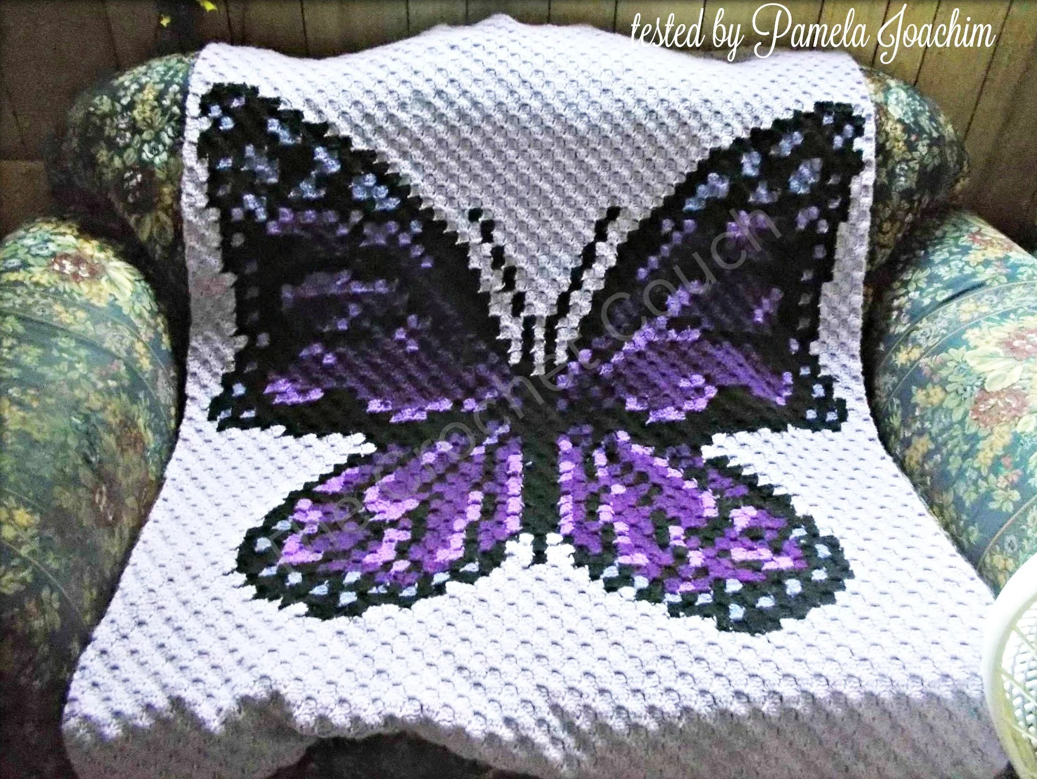 A crochet afghan featuring a large purple butterfly with intricate wing details, displayed on a floral armchair.