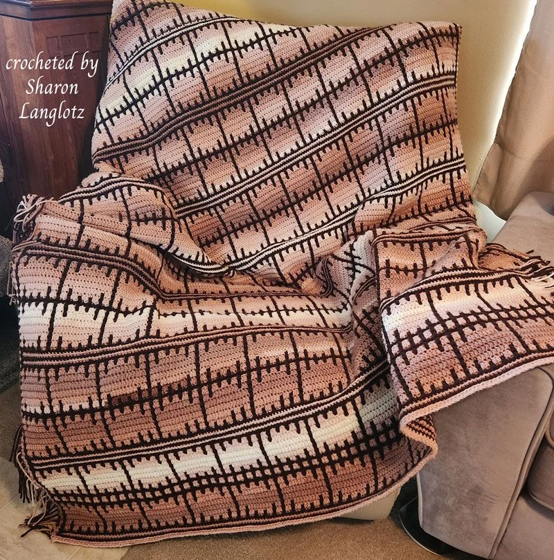 A handmade crochet afghan featuring a geometric woven lattice design in warm earthy tones, draped over a chair.