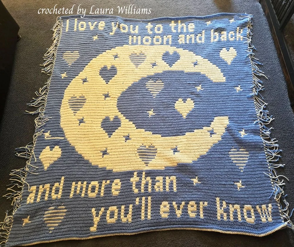 Crocheted afghan featuring a large crescent moon with hearts and stars on a blue background