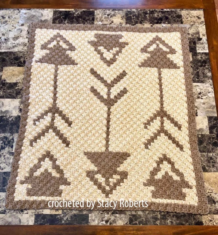Corner-to-corner baby afghan featuring a central vertical arrow flanked by geometric arrow designs on a cream and taupe background. Crocheted and bordered in neutral tones.