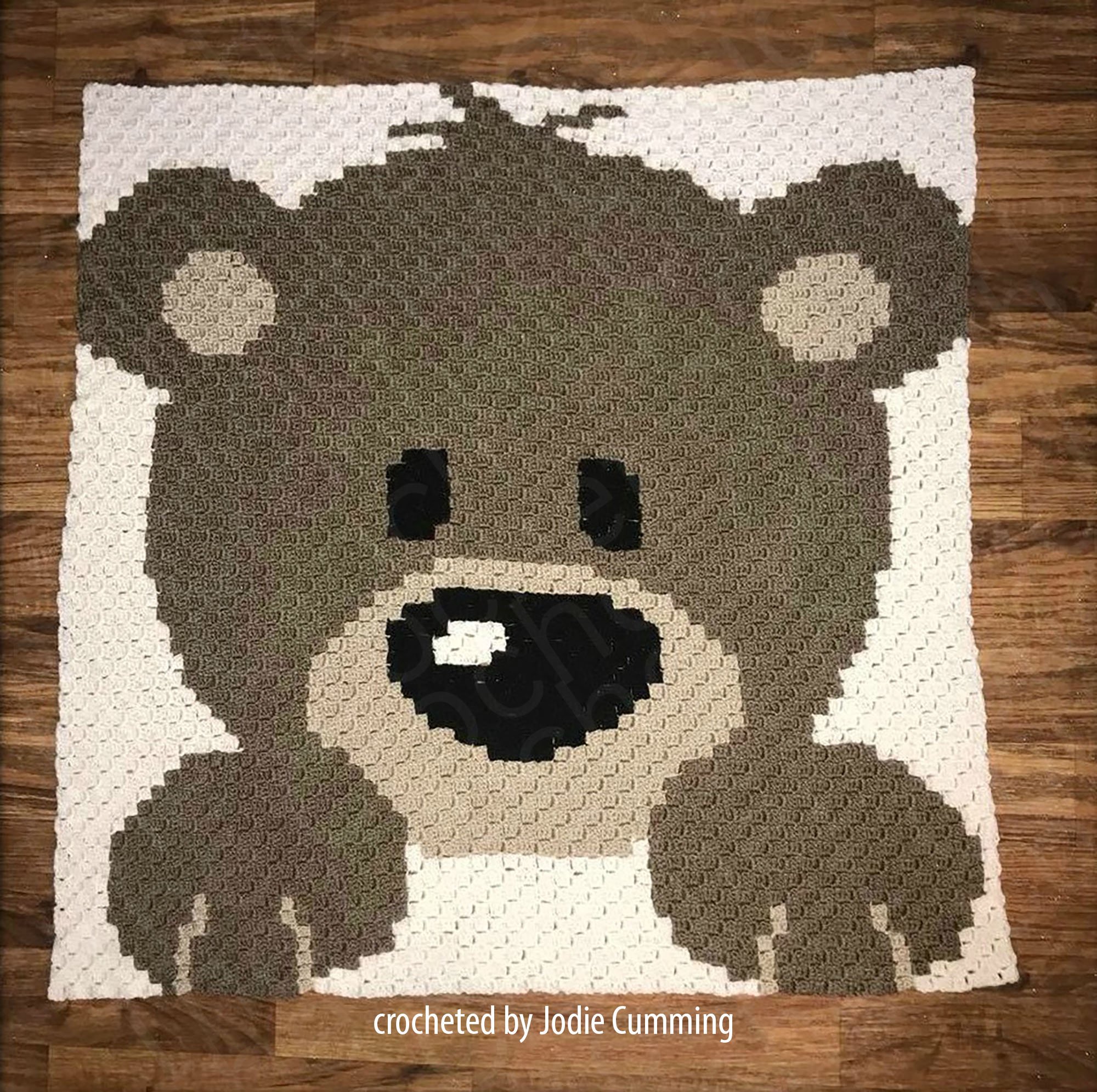 A crocheted afghan featuring a cute baby bear design made in a C2C pattern. The bear is in shades of brown and beige with a playful expression.