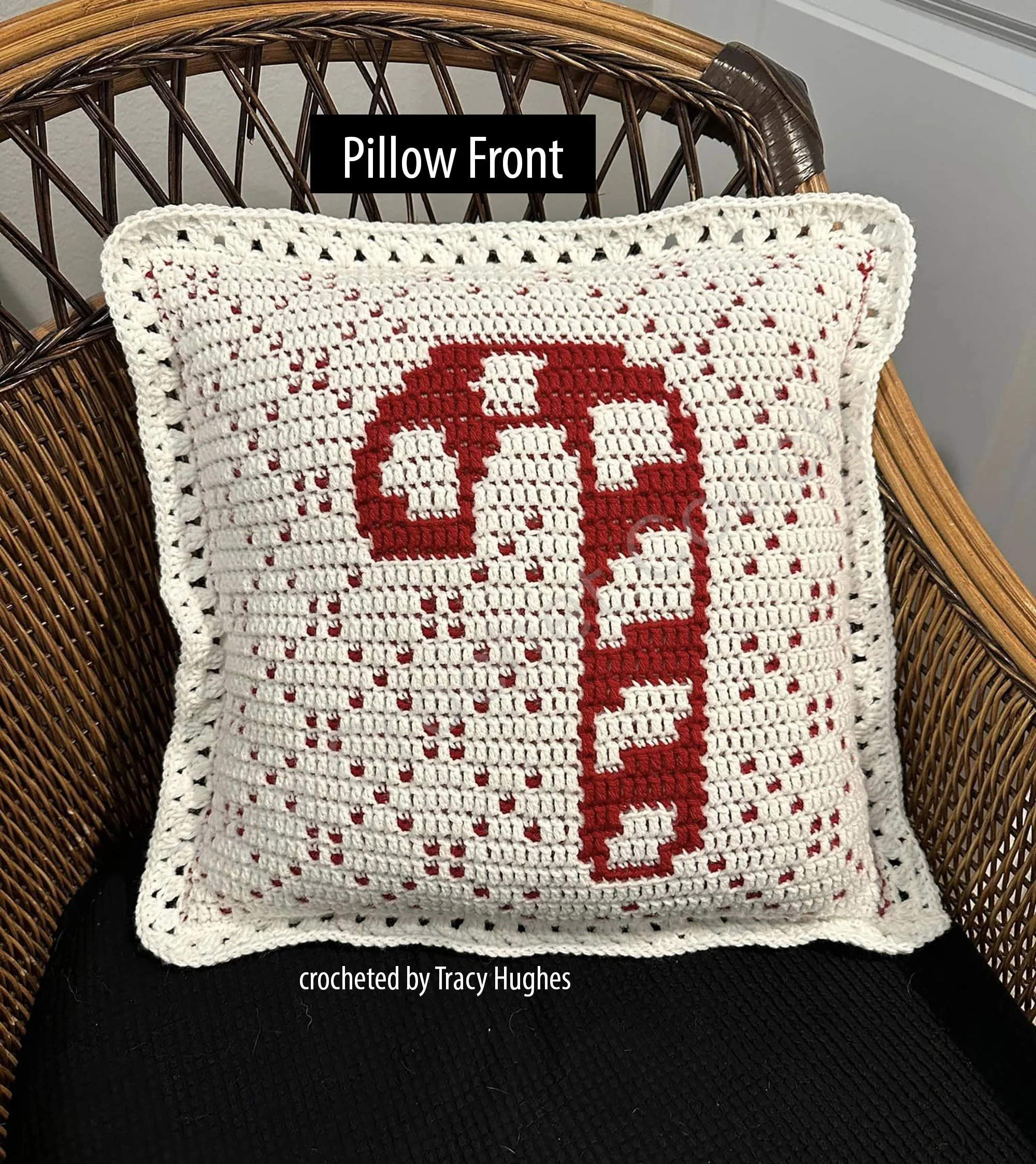 A handmade crochet pillow featuring a candy cane design on a white background, displayed on a wicker chair. The red and white candy cane pattern adds a festive, holiday feel.
