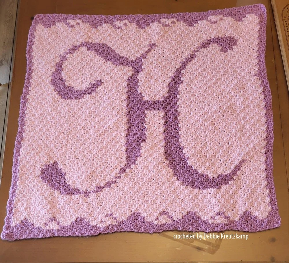 A handmade crochet baby afghan featuring the letter H in a soft two-tone color scheme, made using the corner-to-corner technique.