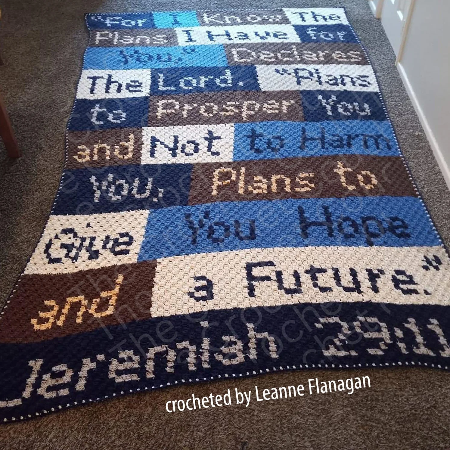 Handmade crochet blanket featuring the Jeremiah 29:11 Bible verse in blue, brown, and cream-colored blocks, displayed on a carpeted floor.