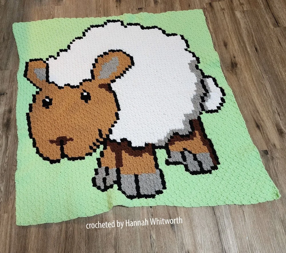 Baby Afghan depicting a white sheep on a light green background .  Afghan is laying on a laminate wood floor